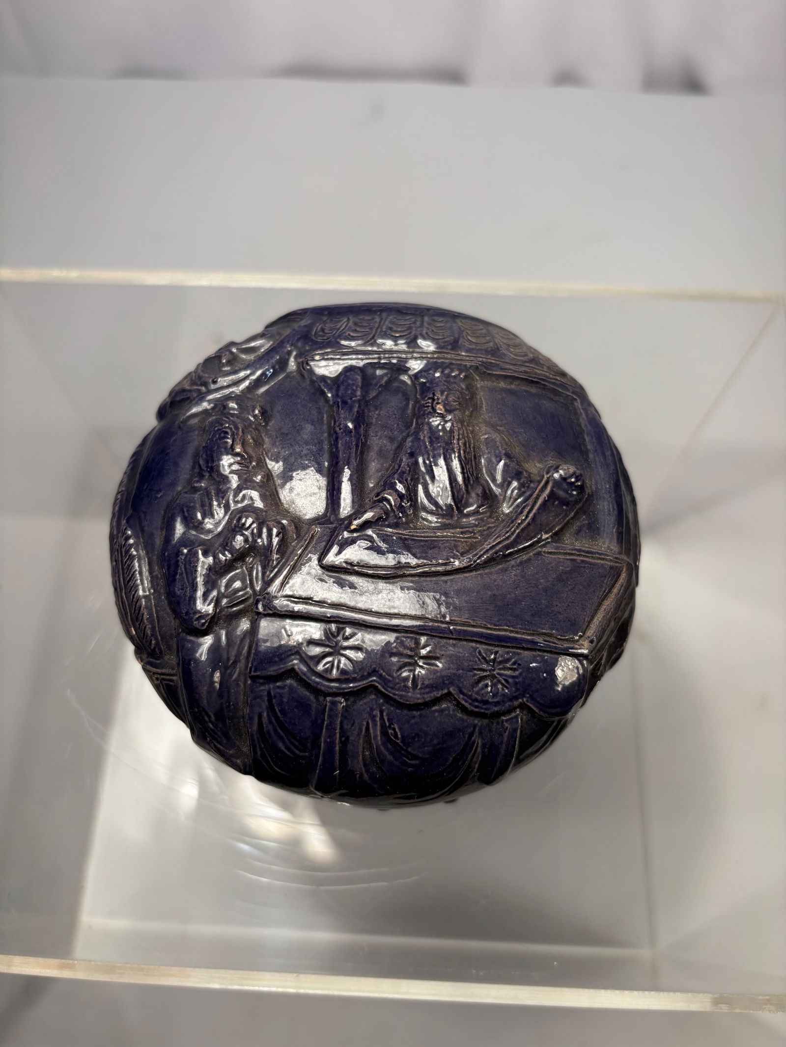 A Chinese Purple-Glazed Molded Figural Box: Qing dynasty(1644-1912) ; A Chinese purple-glazed molded ceramic box, likely dating to the late Qing dynasty, the cover finely modeled in low relief with a figural scene of two scholars beneath a pavi