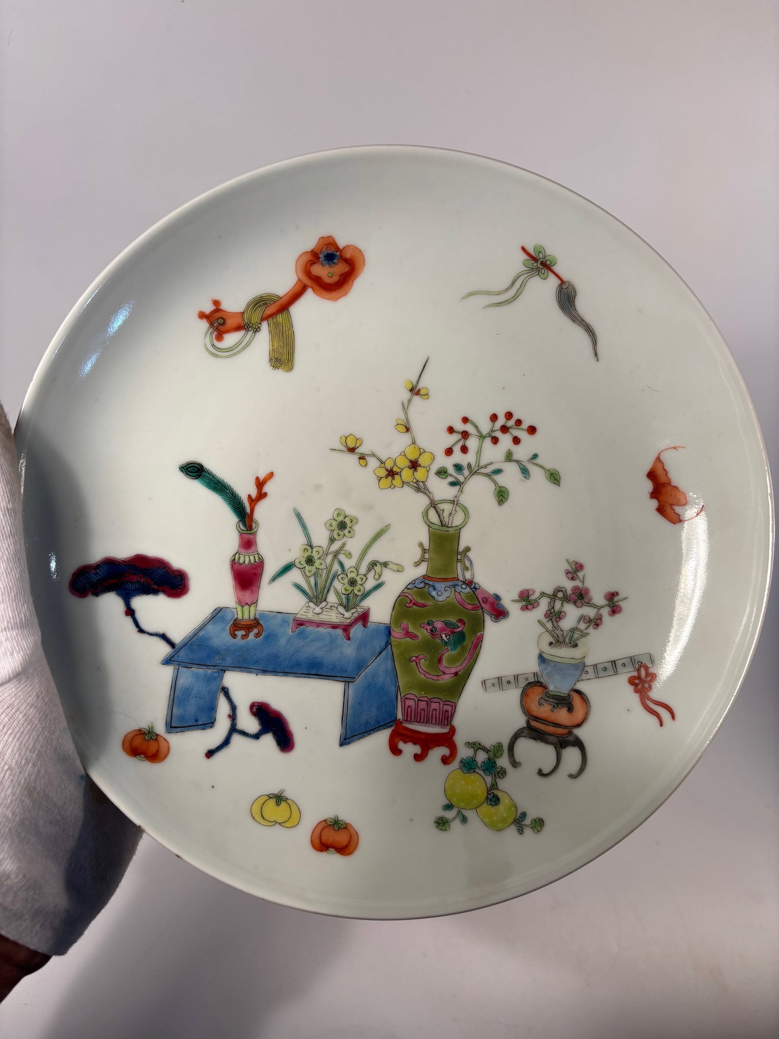 A Chinese famille rose plate: Qing dynasty(1644-1912); Still life with vases, tables, and symbolic scholar's objects. Dimensions?Diameter: 9 inches