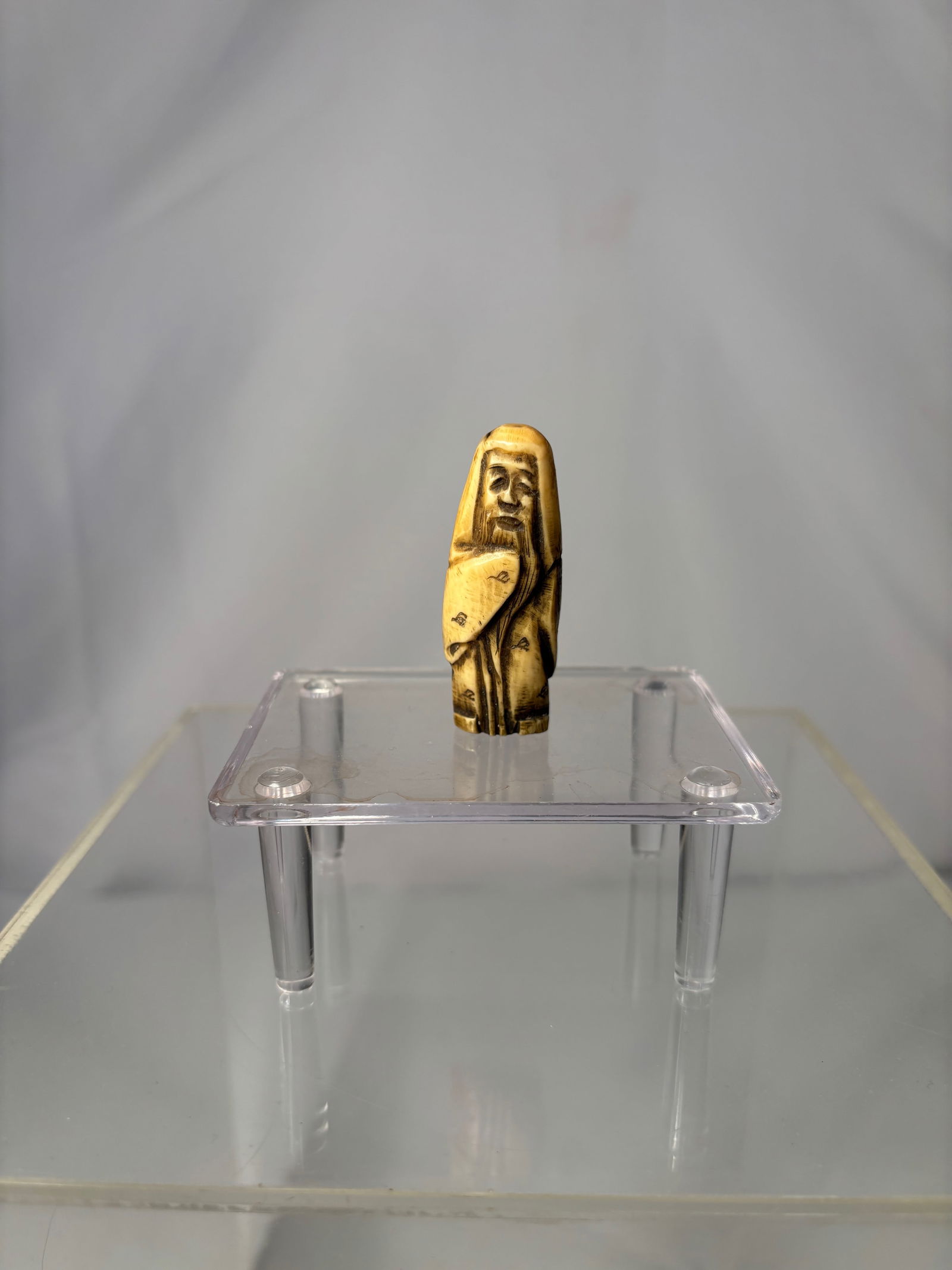 A Japanese Figural Netsuke, Carved Bone Standing Figure, Signed (Hisakazu / Ky?ichi): 19th century, A Japanese figural netsuke carved from bone, depicting a standing human figure with a humorous expression and stylized features. The carving includes two himotoshi to the reverse,