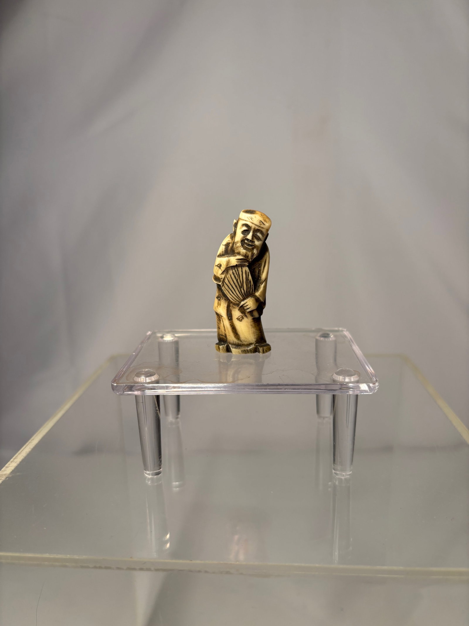 A Japanese Figural Netsuke, Carved Bone Standing Figure, Signed (Hisakazu / Ky?ichi): 19th century, A Japanese figural netsuke carved from bone, depicting a standing human figure with a humorous expression and stylized features. The carving includes two himotoshi to the reverse,