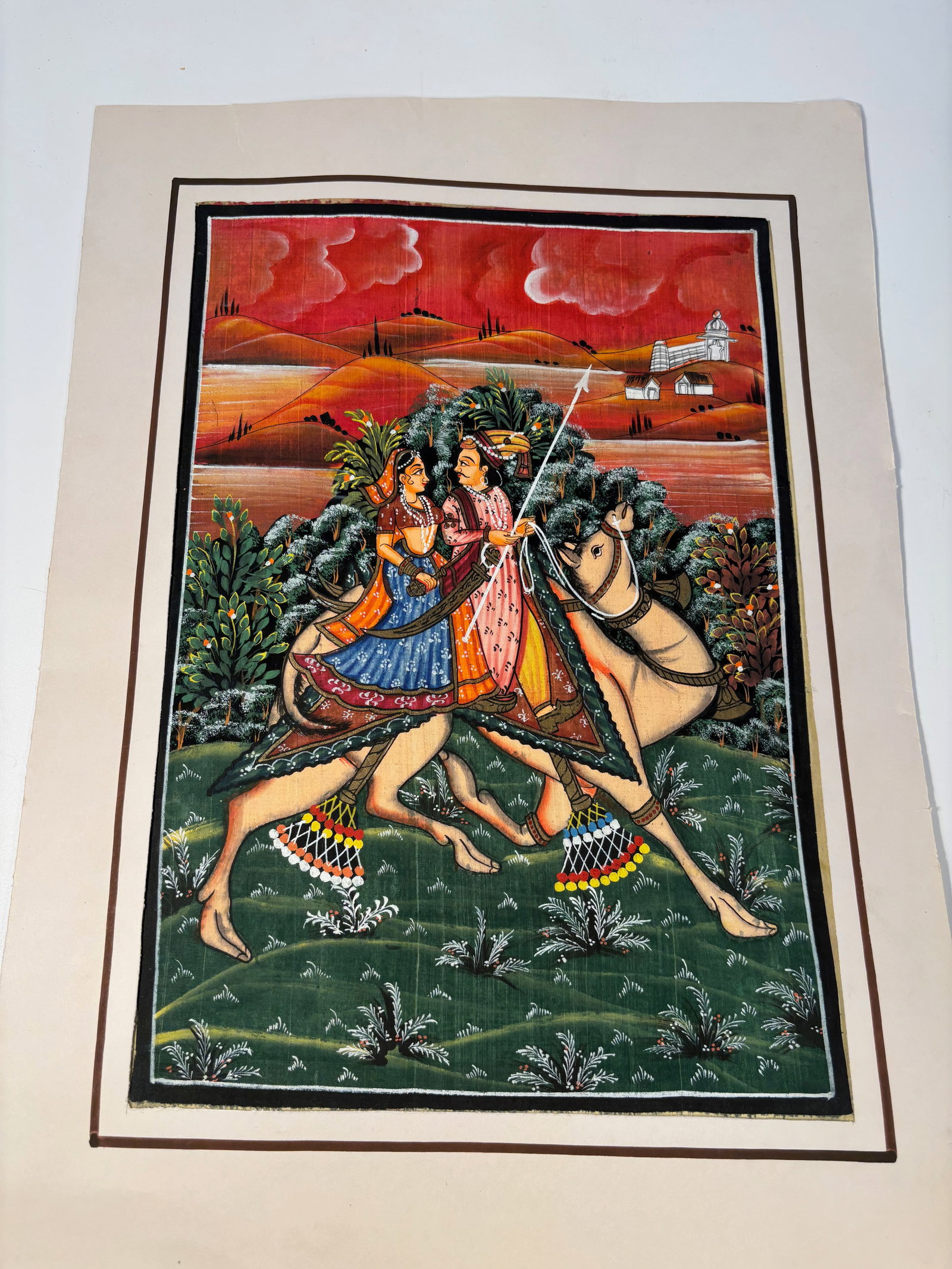 Indian Gouache Miniature of a Noble Couple on Camelback, Rajasthan: 19th/20th Century,Gouache and ink on silk/paper, brightly painted in rich pigments, depicting a noble couple riding a caparisoned camel through a lush green landscape beneath a vivid red sky with roll