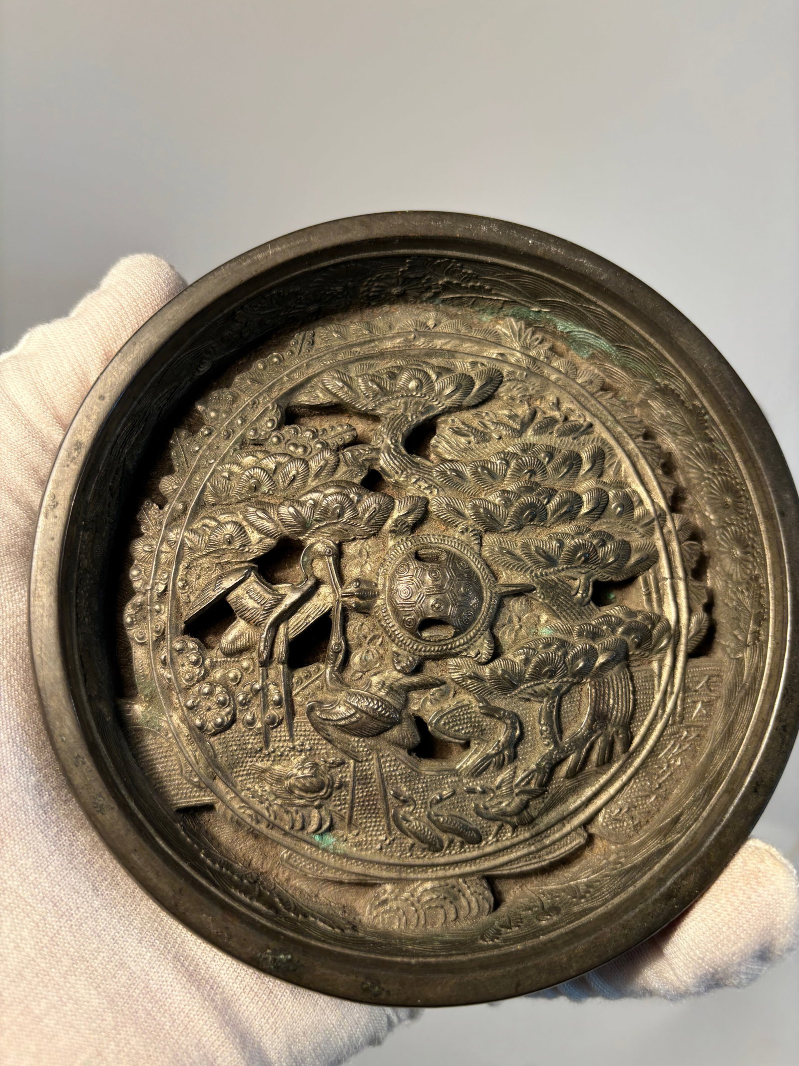 A Japanese silvered bronze mirrors with signature: Edo Period (1603–1868); Cast in high relief with fine detailing, the circular bronze mirror features a central boss surrounded by an elaborate composition of phoenixes in flight amid stylized clouds