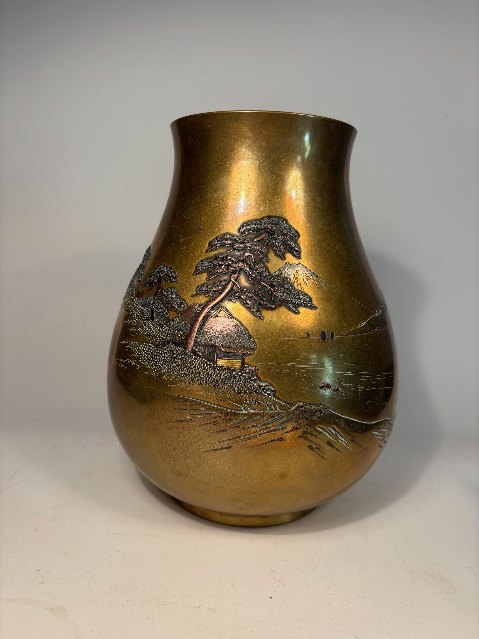 A Japanese gilted Bronze Vase with Landscape Relief, Signed “Ch?gi: Meiji Period (1868–1912), A finely cast in high relief with a detailed landscape depicting traditional thatched-roof houses beneath windswept pine trees, with distant sailboats and Mount Fuji in the