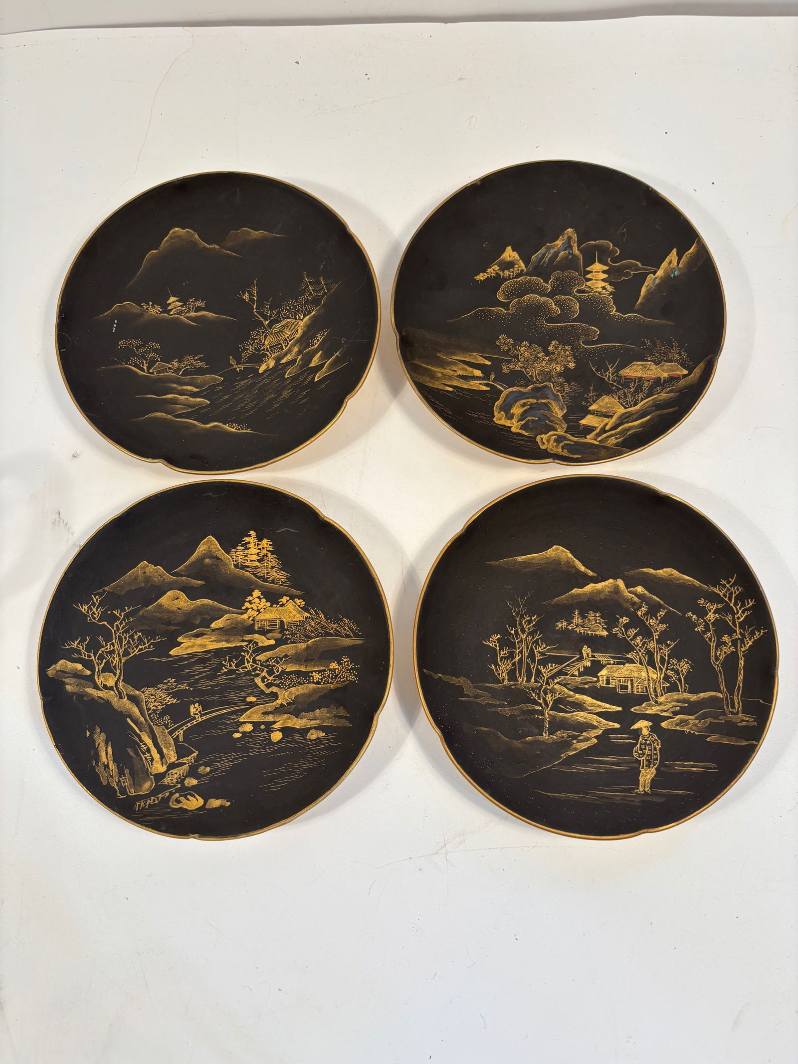 Set of Four Japanese Gold on Black hand painted plates with mark: A group of four early-20th century pieces, each finely decorated with gilt-painted landscape scenes of mountains, trees, and pavilions on a black glazed ground. Dimensions?Diameter: 6.25 inches. Heigh
