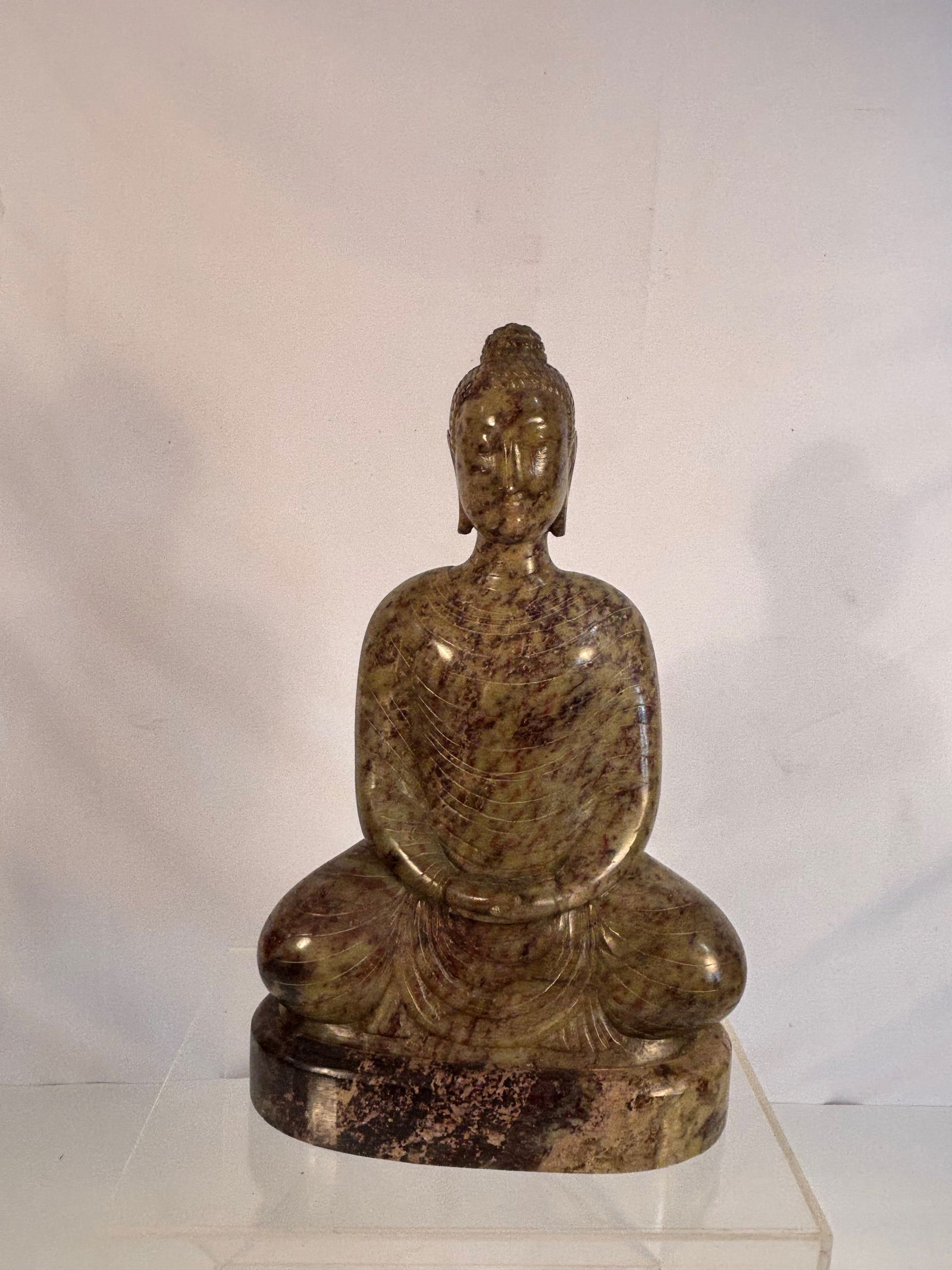 An Asian Carved Stone Seated Buddha: Late 19th to Early 20th century. A carved stone figure of the Buddha, The figure is depicted seated in meditation (dhyana mudra) on an integral oval base, with elongated features, downcast eyes, and l