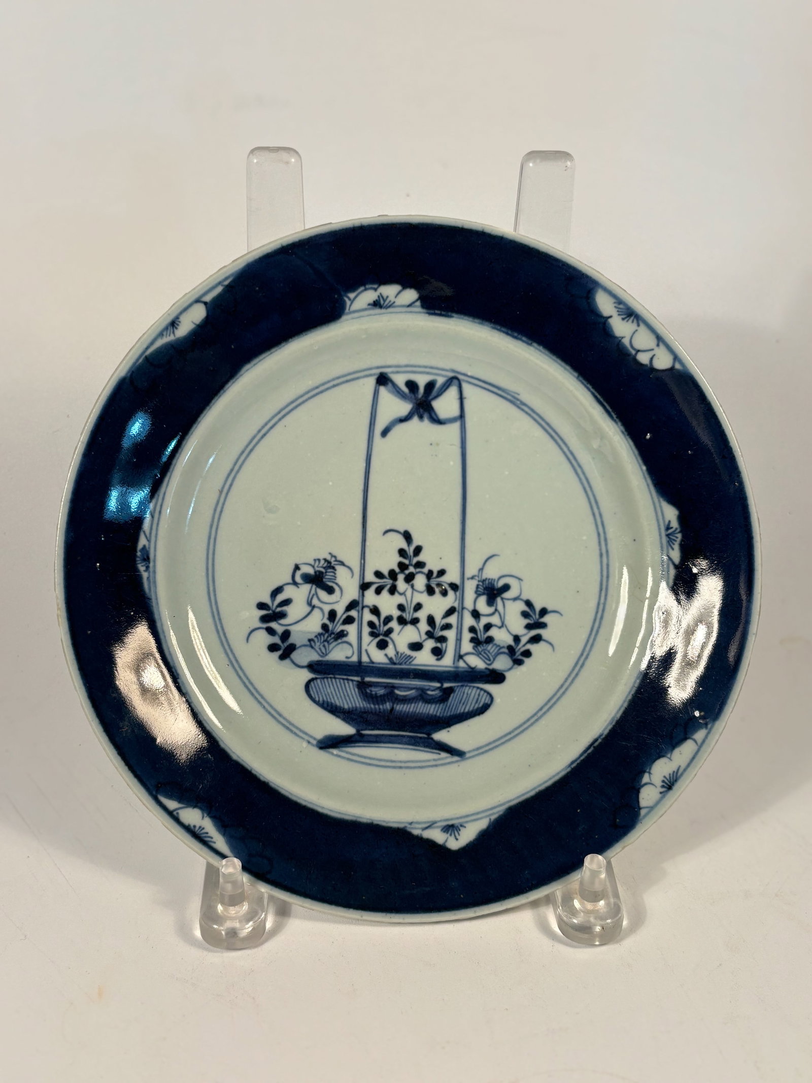 A Chinese blue and white porcelain plate with double circle mark: 18th century ; The hanging flower basket (often suspended from a ribbon or rod) is a classic Kangxi period (1662–1722) decorative motif. This finely painted Chinese porcelain plate features a centra