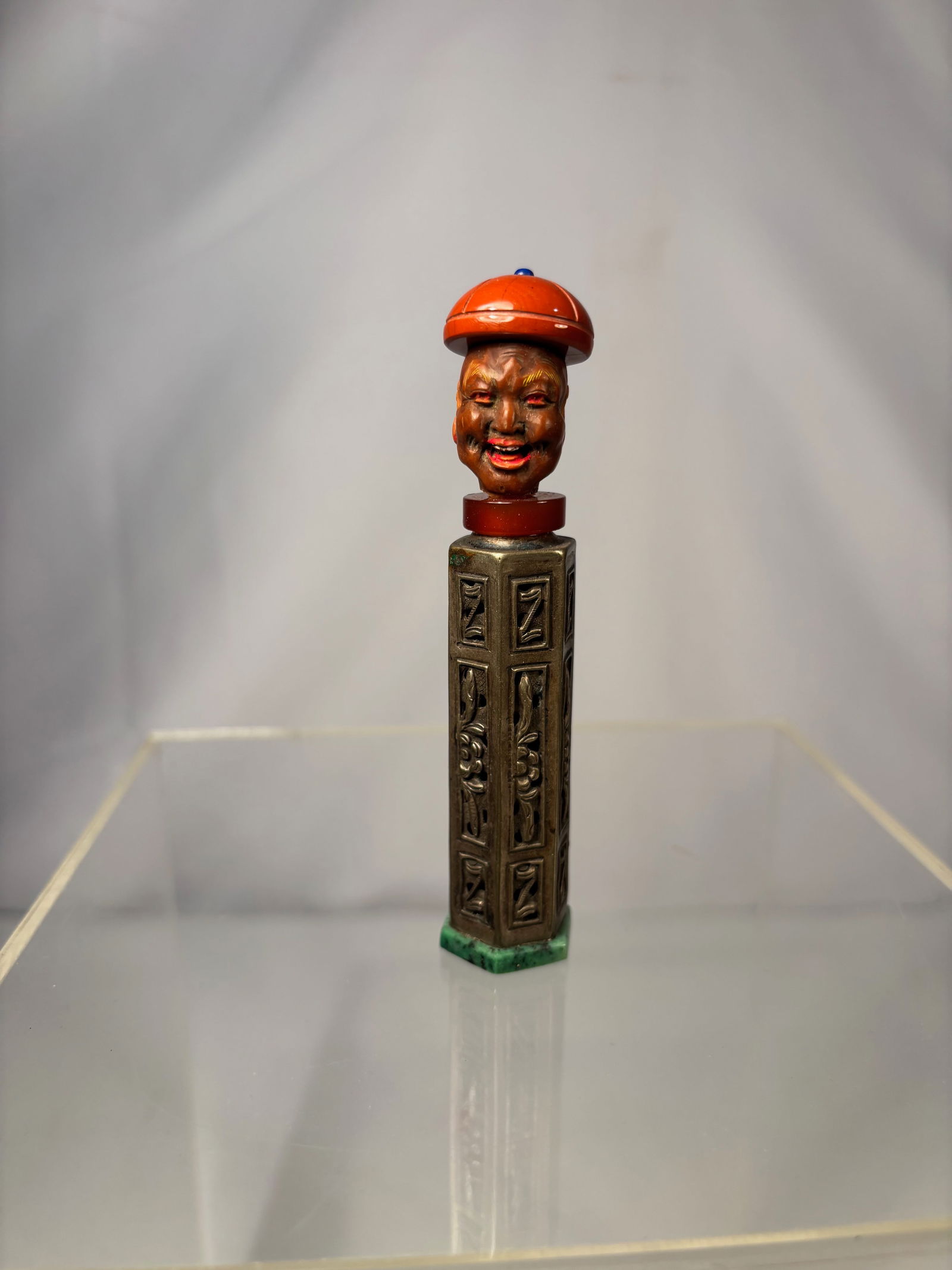 A Chinese composite snuff bottle, late Qing dynasty, circa 1880–1920: The bottle with a silver body, cast and chased in archaistic panel form, raised on a hexagonal green hardstone base (likely nephrite or serpentine). The neck fitted with a red stone or glass collar. T