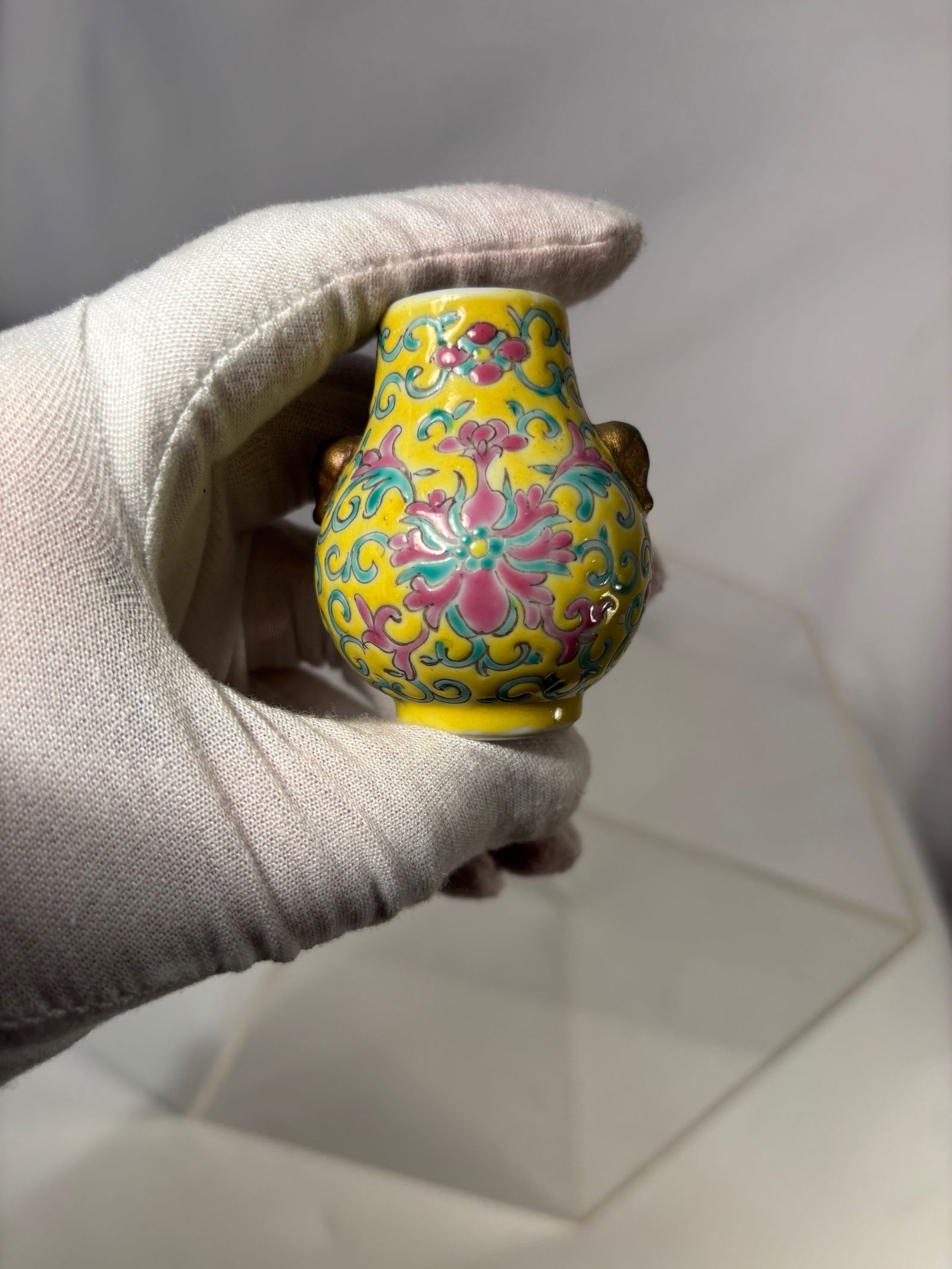 A Chinese Enameled Porcelain Miniature Vase with Gilt Mask Handles, Marked China: Small porcelain vase of bulbous form decorated with colorful scrolling foliate motifs on a bright yellow ground. Applied gilt mask handles to each side. Interior glazed white. Base marked “China.&rd