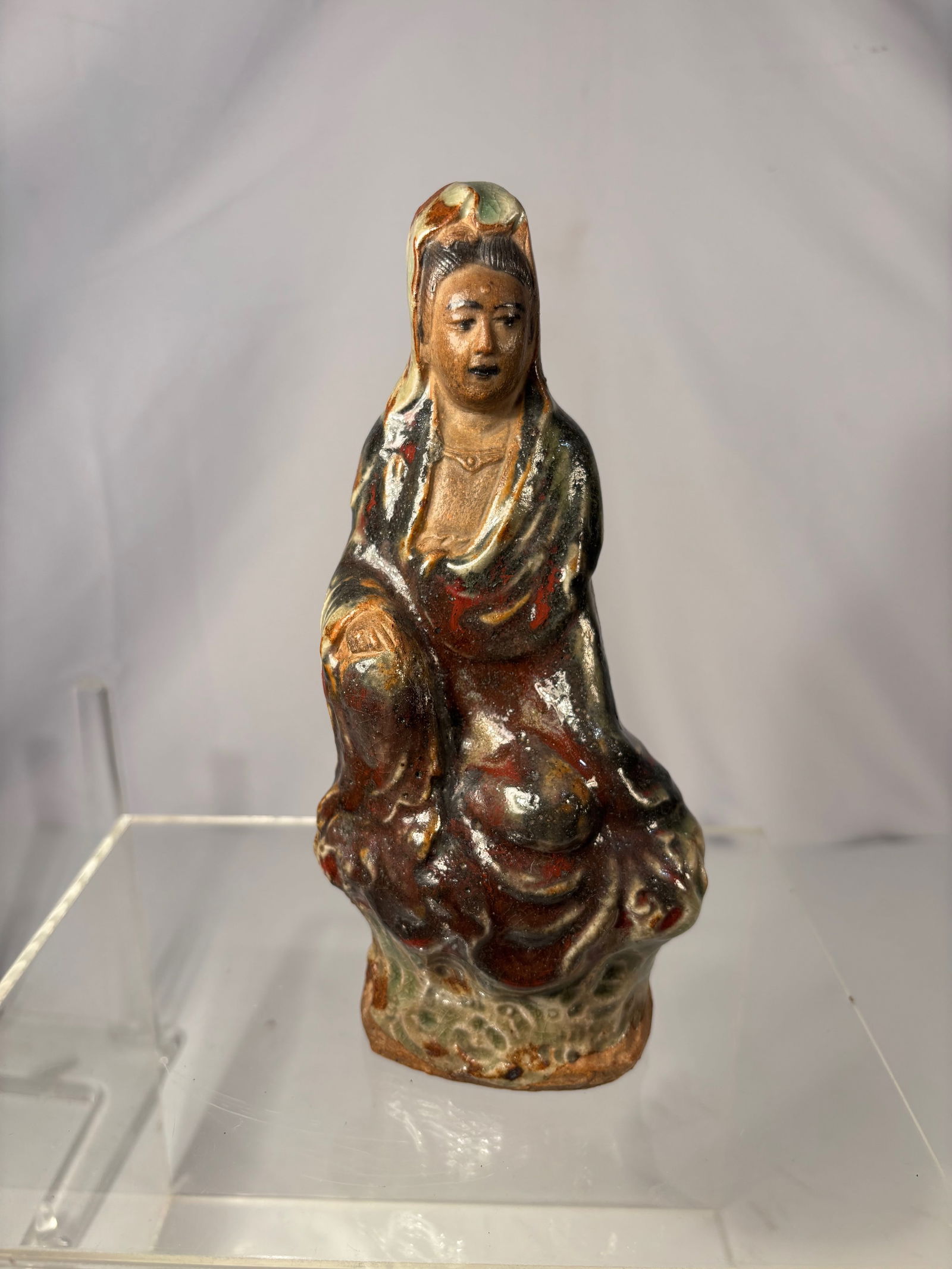 A Chinese Shiwan Polychrome-Glazed Pottery Figure of Guanyin: Qing dynasty(1644-1912) ; The bodhisattva is modeled seated in a relaxed pose, the robes rendered with thick, flowing sculptural folds and covered in characteristic Shiwan glazes of chestnut brown, de