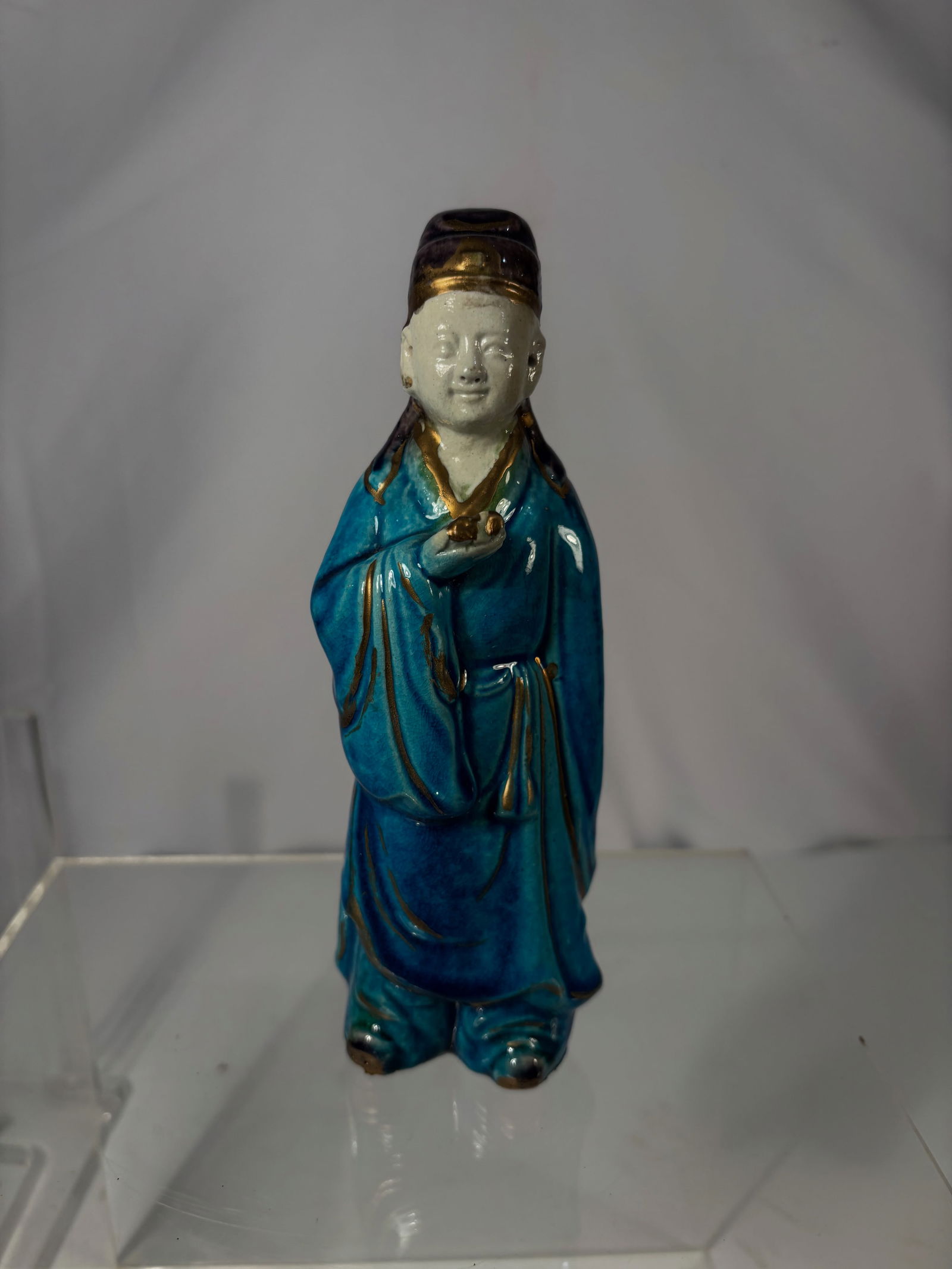 A Chinese Blue-Glazed Porcelain Figure with Gold Highlights: Qing dynasty(1644-1912) ; A Chinese glazed porcelain figure, decorated in rich turquoise and deep blue glazes with gilt accents. The standing figure is shown holding a small object in one hand and wea