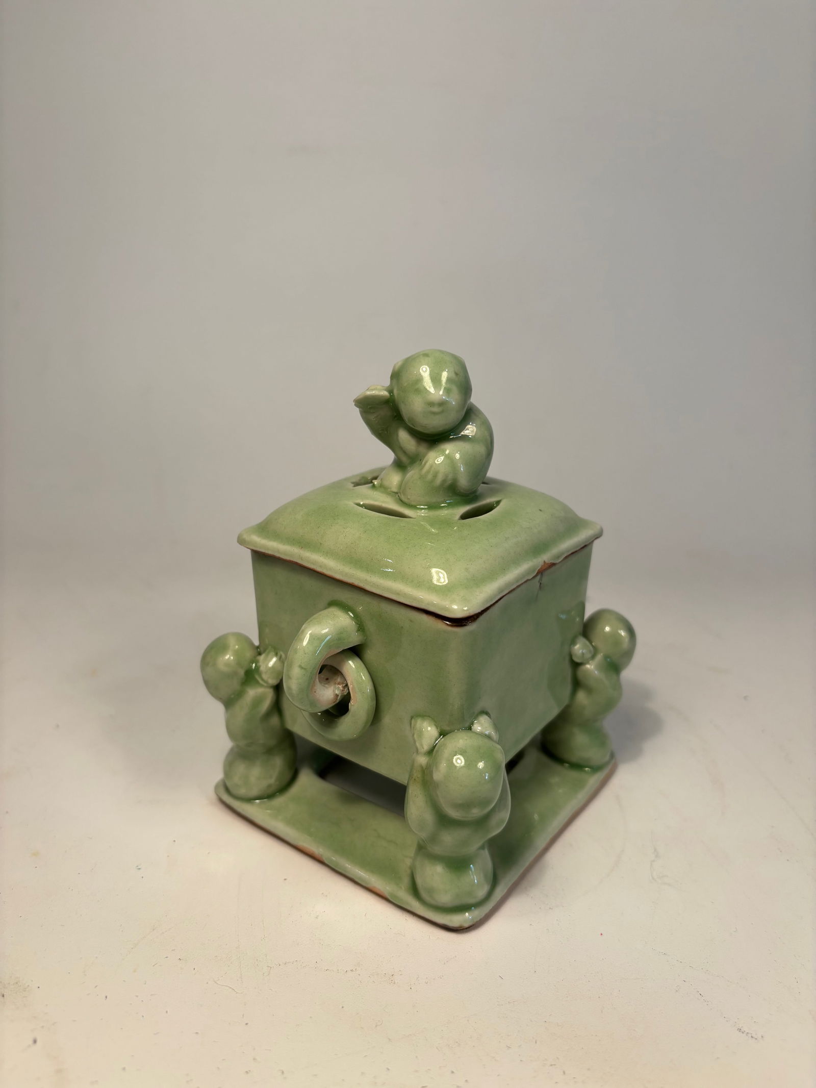 A Japanese Green-Glazed Figural Incense Burner: Late 19th century -early 20th century, A Japanese green-glazed ceramic k?ro (incense burner), Of square form, the piece is supported on four stylized zoomorphic or humanoid feet, with a domed lid surm