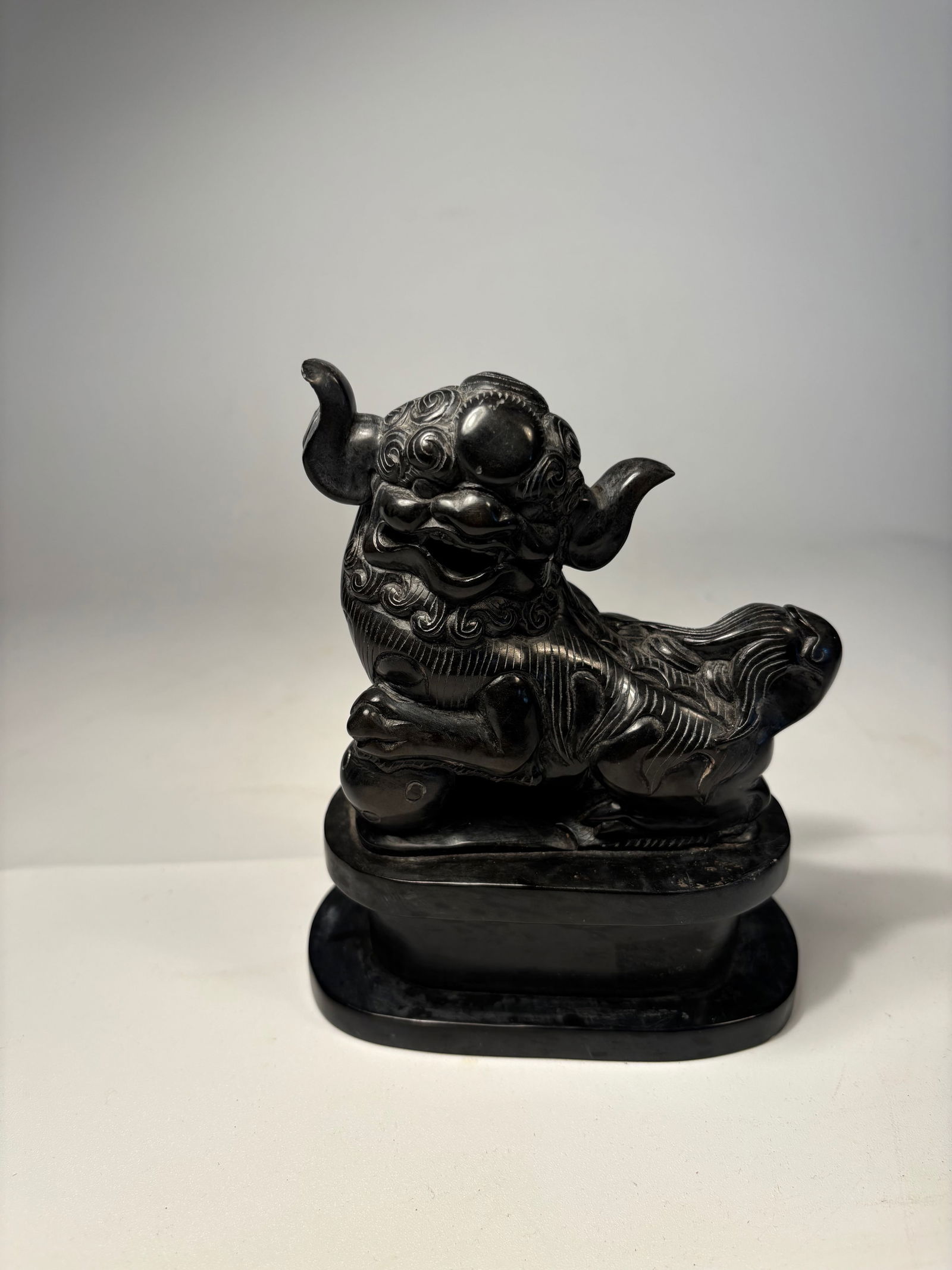 A Chinese carved stone foo dog: early 20th century; depicted in a reclining position with raised head and elaborate curling mane. The figure has exaggerated features — bulging eyes, curling eyebrows, and stylized fur . ?Dimensions
