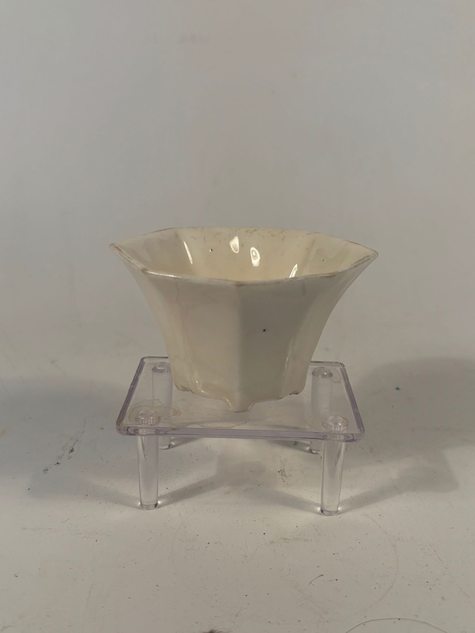 A Chinese Blanc-de-Chine Hexagonal Cup: Qing dynasty(1644-1912); Of faceted hexagonal form with six bracket-lobed sides, raised on three short ruyi-form feet. The glossy white glaze typical of Dehua ware. An impressed or incised mark to the