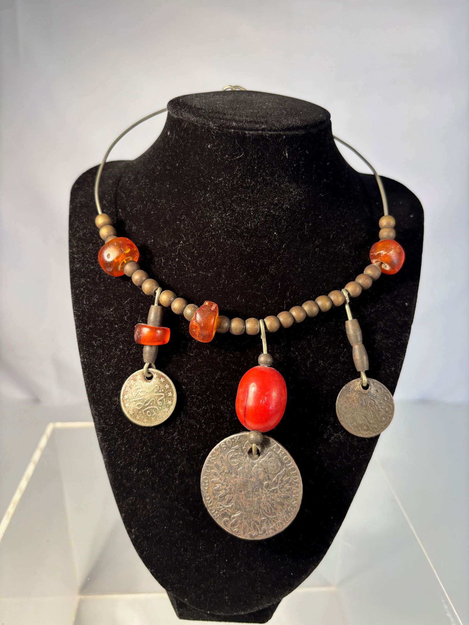 A necklace with Amber Beads and Silver Maria Theresa Thaler Coins: An antique necklace composed of natural amber and red coral beads, interspaced with smaller wooden beads, and suspended with silver Maria Theresa Thaler trade coins. The Maria Theresa Thaler, first mi