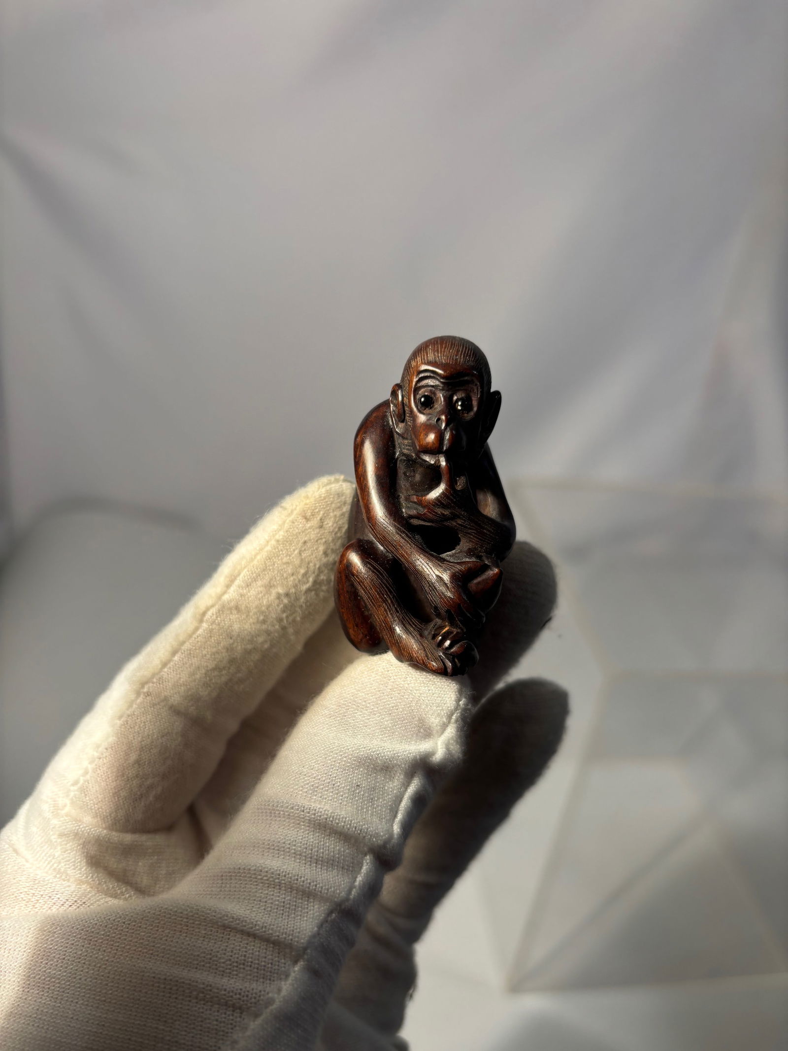 A Carved Hardwood Monkey Netsuke Style Figure with Seal Mark, 20th Century: Finely carved hardwood figure depicting a seated monkey in a contemplative pose, one hand raised toward its mouth in a thoughtful gesture. The sculpture features detailed facial expression, incised ha