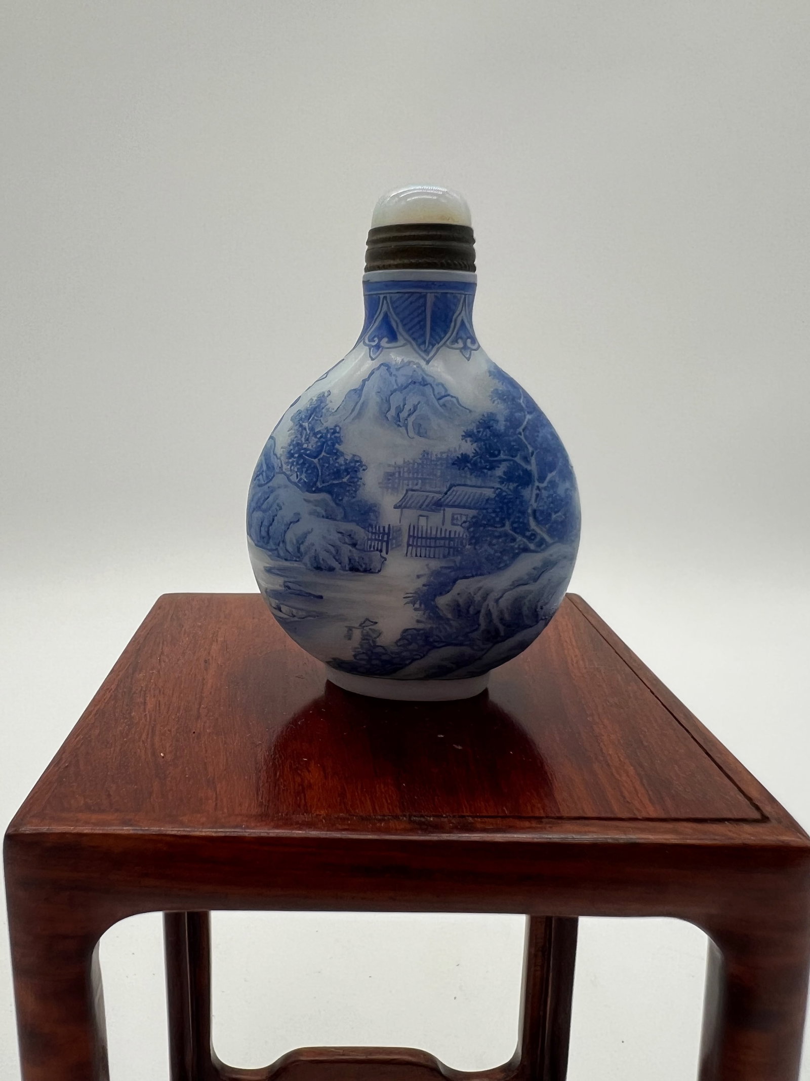 A Chinese blue enamel glass snuff bottle with QianLong Four-Character Mark: Qing Dynasty (1644-1912); The design on this enamel snuff bottle features a classic Chinese landscape scene, which includes elements such as mountains, trees, a river, and traditional architecture, su