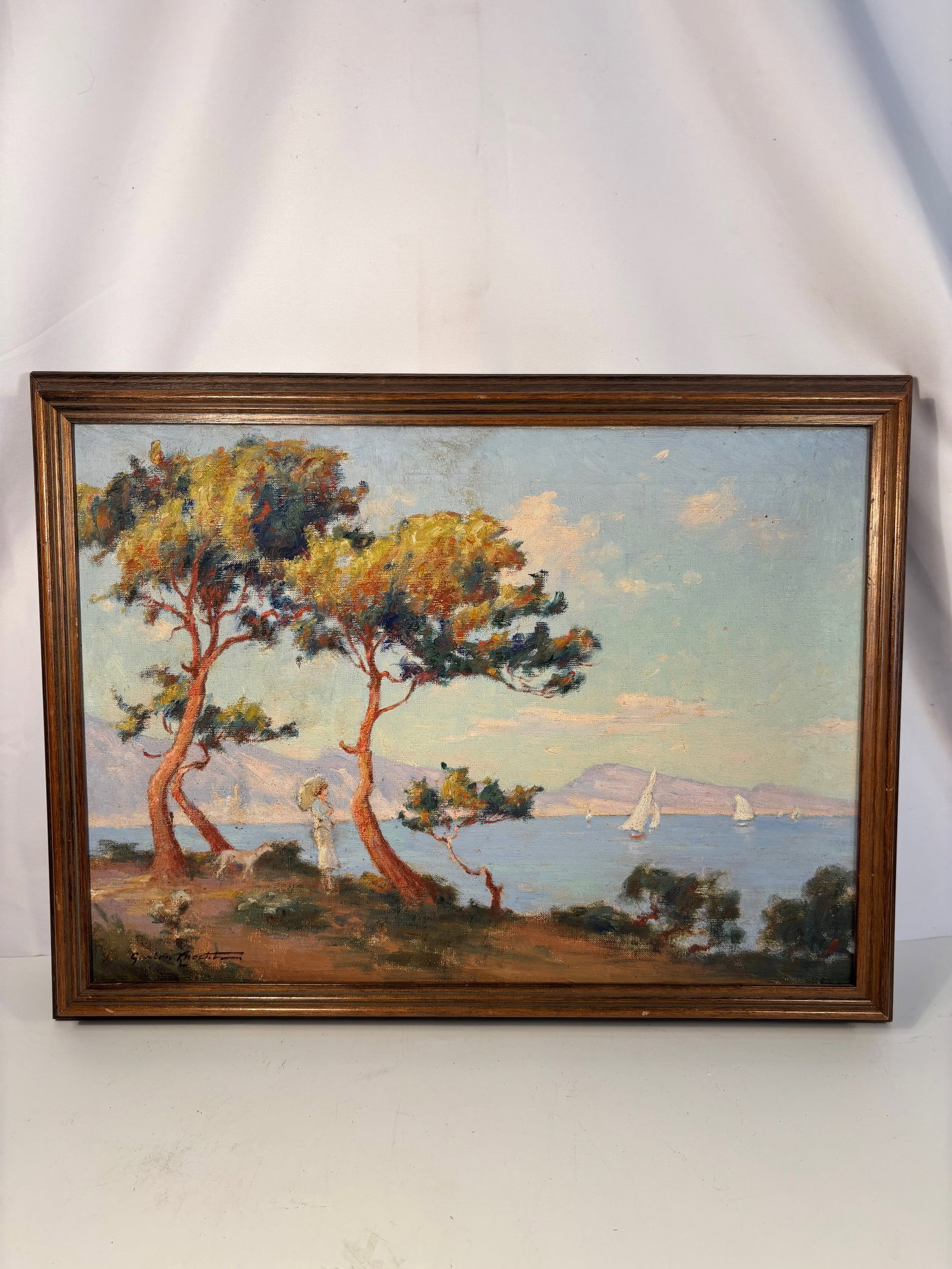 Gaston Knecht (1875 – 1968, French) Lady with Dog beneath the Trees, Mediterranean Coast,Oil on: A luminous coastal landscape depicting a lady with her dog beneath two windswept trees overlooking the tranquil Mediterranean. Painted with lively impasto and a radiant palette of blues, greens, and o