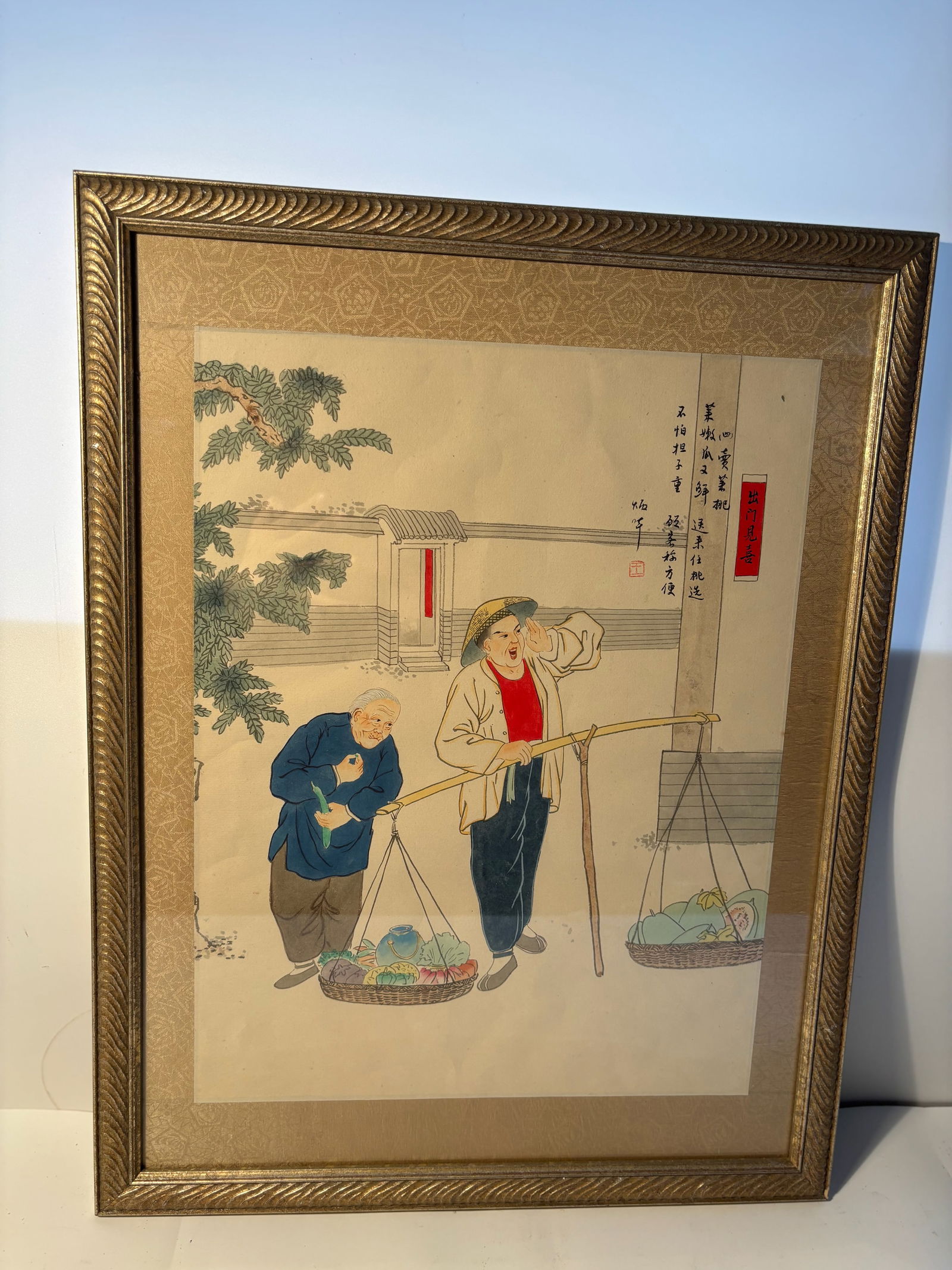 A Chinese water color painting in Frame signed Wang Binghua: This framed artwork depicts two individuals, likely farmers or street vendors, carrying baskets of goods on a traditional shoulder pole. The piece is painted in a delicate and detailed style, typical