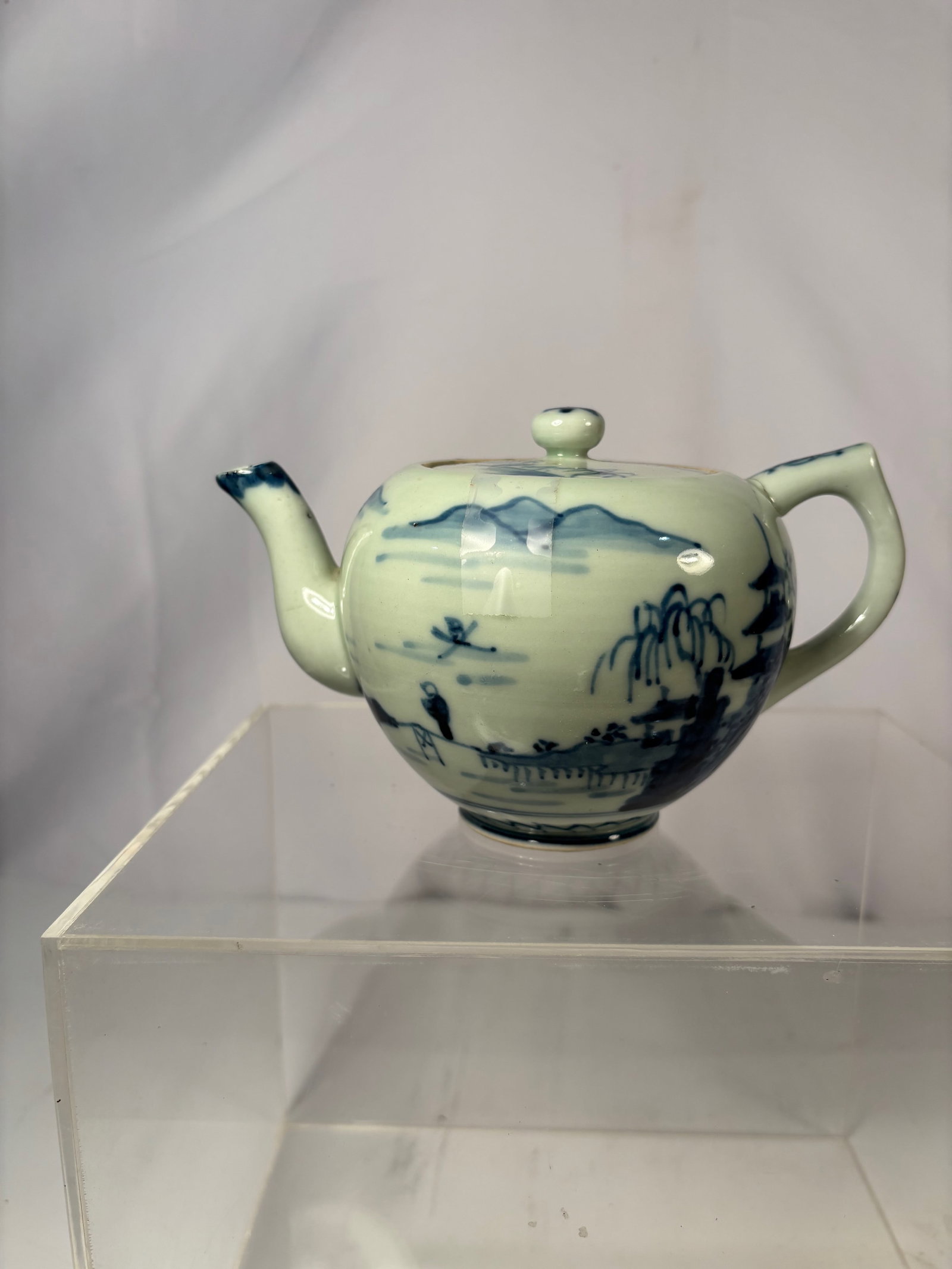 A Japanese Arita Blue-and-White Porcelain Teapot, Late Edo to Early Meiji Period (circa 1850–1880): Of globular form with loop handle and short spout, decorated in underglaze blue with a continuous landscape scene of mountains, willow trees, and a pavilion by water. The base painted with a blue zig-