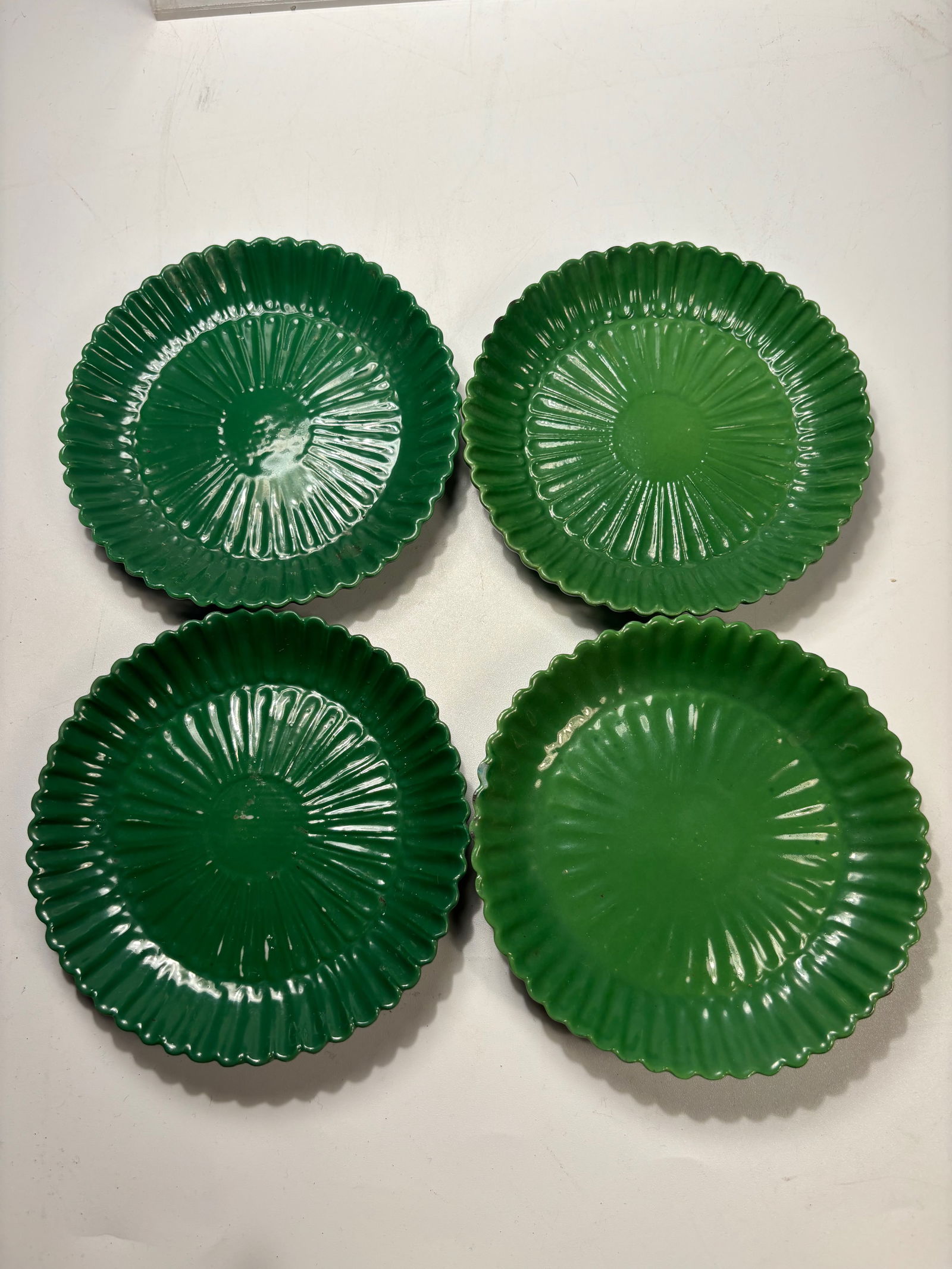 Set of Four Italian Green-Glazed Ceramic Dishes: A set of four Italian green-glazed ceramic dishes, each molded with radiating rib decoration and a scalloped rim. The bases are marked “ITALY.” The pieces display a glossy green glaze with sli