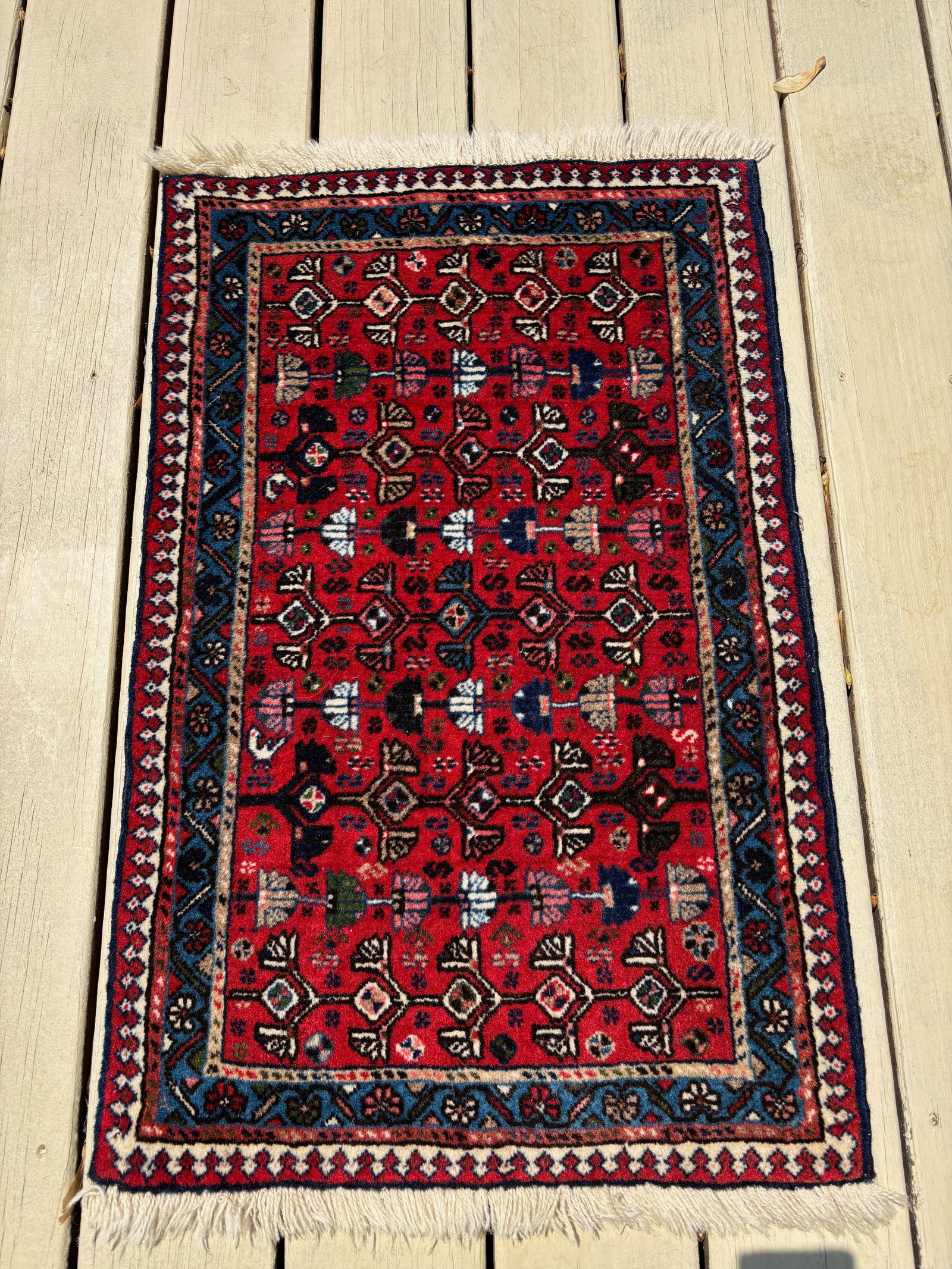 A Persian Qashqai 100% wool Rug, Southwest Iran: Probably Early 20th Century; A hand-knotted Qashqai tribal rug, early 20th century, from southwest Iran. The deep red field is filled with an array of repeating diamond and floral motifs, framed by mu