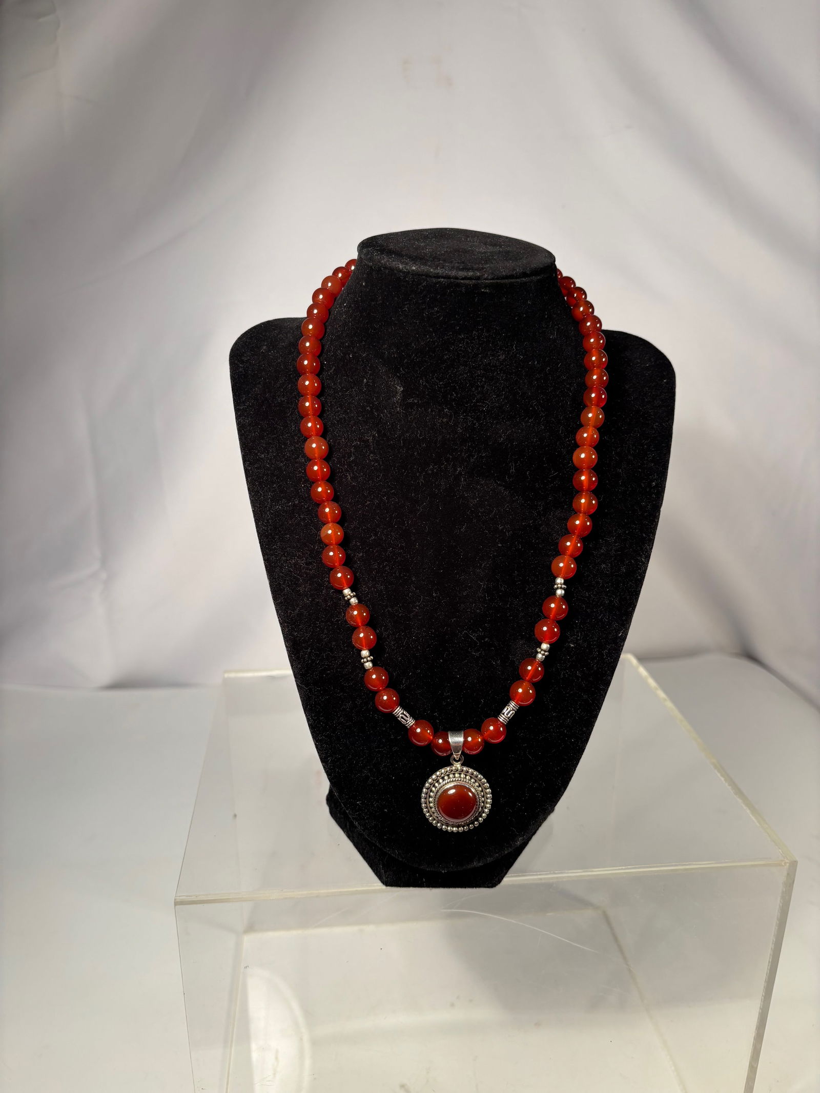 A Carnelian Bead Necklace with Cabochon Pendant: This necklace is composed of polished round carnelian beads, displaying rich reddish-orange to deep amber tones with natural translucency and internal variation. The beads are evenly sized and