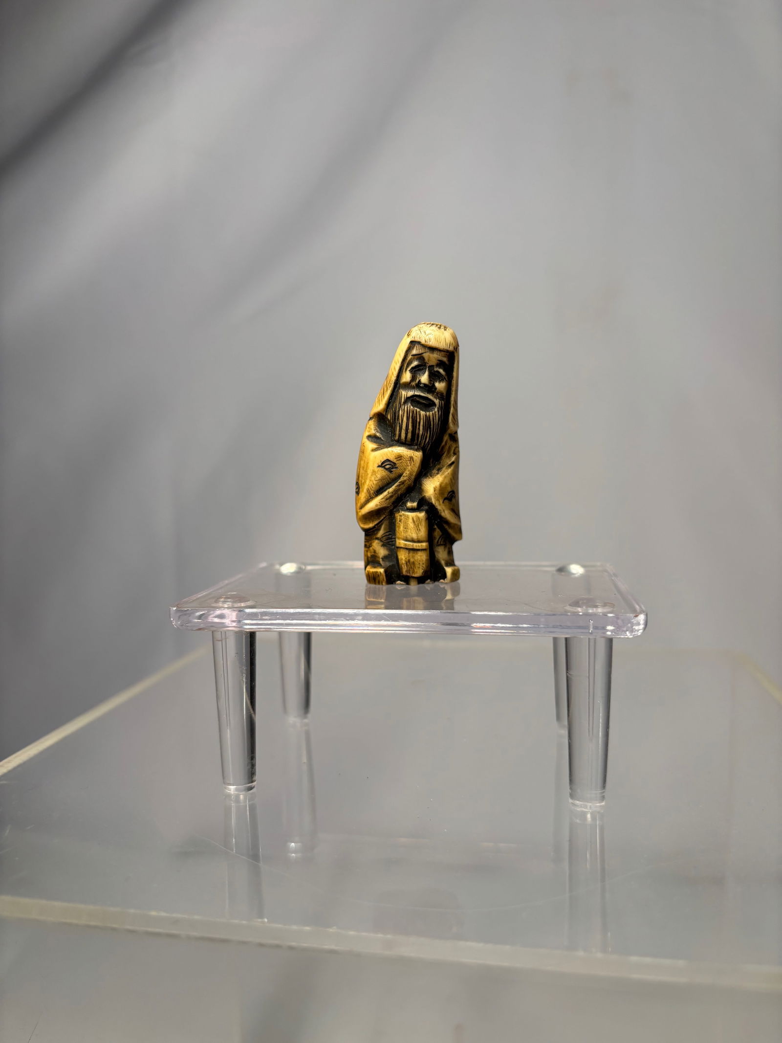 A Japanese Figural Netsuke, Carved Bone Standing Figure, Signed (Hisakazu / Ky?ichi): 19th century, A Japanese figural netsuke carved from bone, depicting a standing human figure with a humorous expression and stylized features. The carving includes two himotoshi to the reverse,