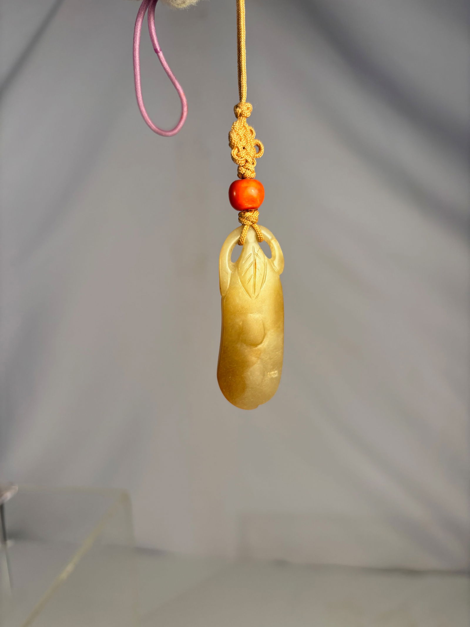A Chinese Nephrite yellow Jade Carved Pendant with Leaf Motif: A Chinese yellow nephrite jade pendant of elongated form, carved with a stylized leaf motif at the pierced top and subtle relief decoration on the body. The stone displays a warm yellow to honey-brown