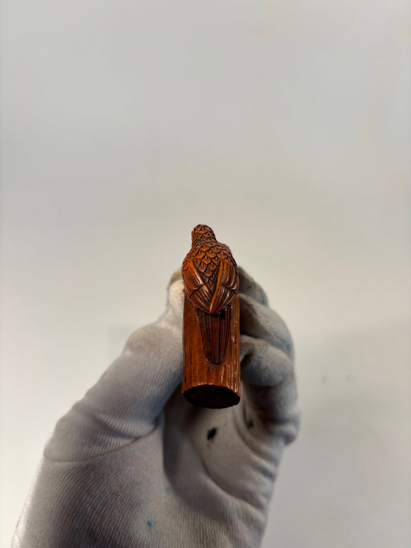 A Japanese Boxwood Netsuke of a Bird on a Branch, Signed Gyokush: Meiji Period or later (late 19th–early 20th century); Finely carved from a single piece of boxwood, the netsuke depicts a bird poised on a gnarled tree branch, its head lowered in a pecking posture.