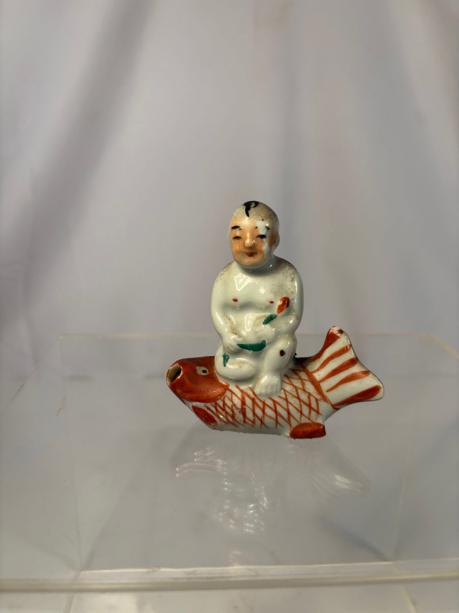 A Chinese Porcelain Figure of a Boy Riding a Carp: Qing dyansty(1644-1912);Charming and finely modeled, the figure depicts a young boy seated atop a red carp, symbolizing prosperity and success. Decorated in overglaze enamels of iron-red, green, and b