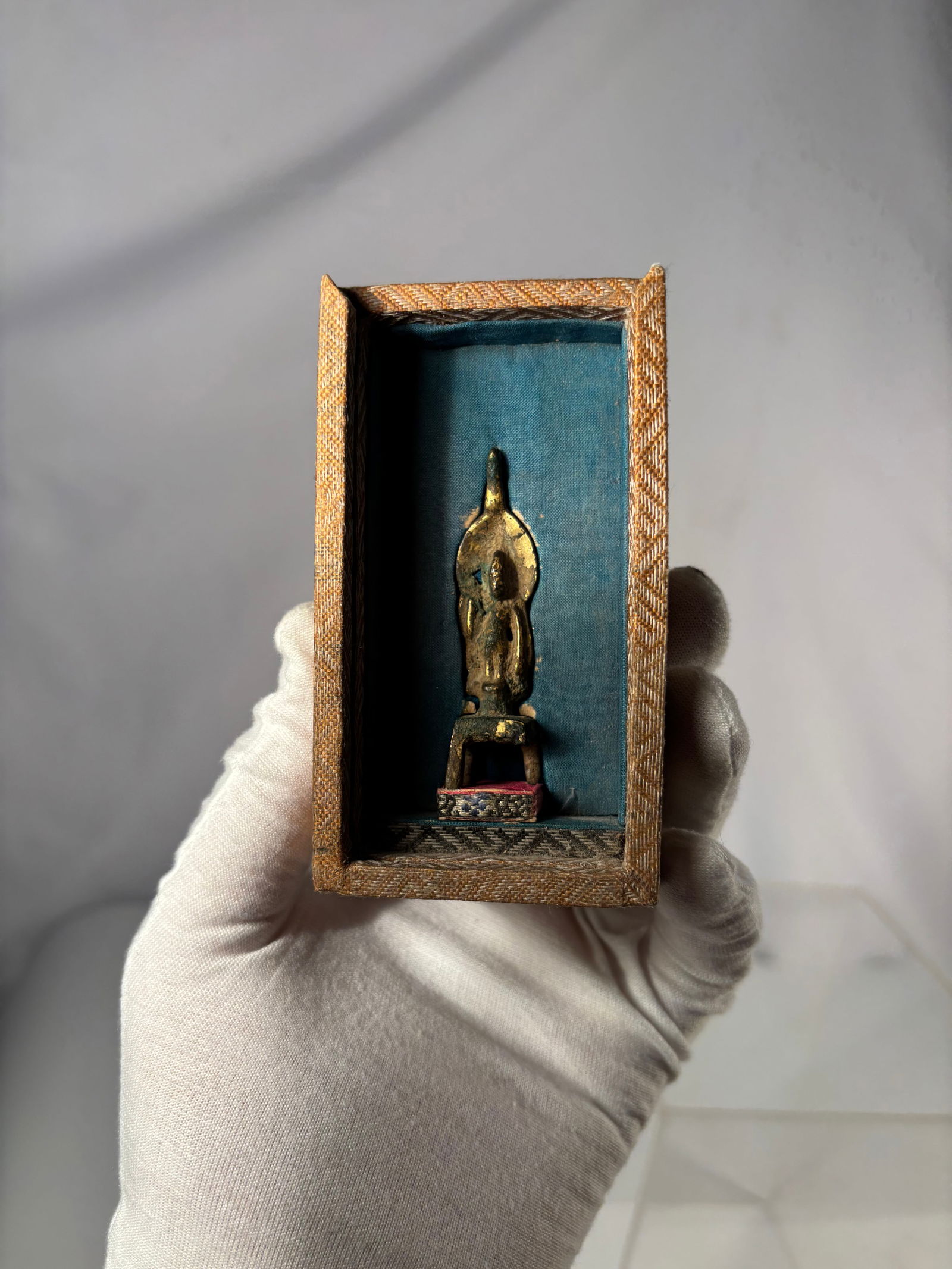 Tibetan/Nepalese Early Gilt Bronze Bench-Seated Buddha, 15th–18th Century, with Shrine Box: Early gilt bronze Buddha figure in a bench-seated (“ban deng fo”) posture, likely Tibetan or Nepalese, dating from the 15th to 18th century. Cast in a primitive devotional style with a high re