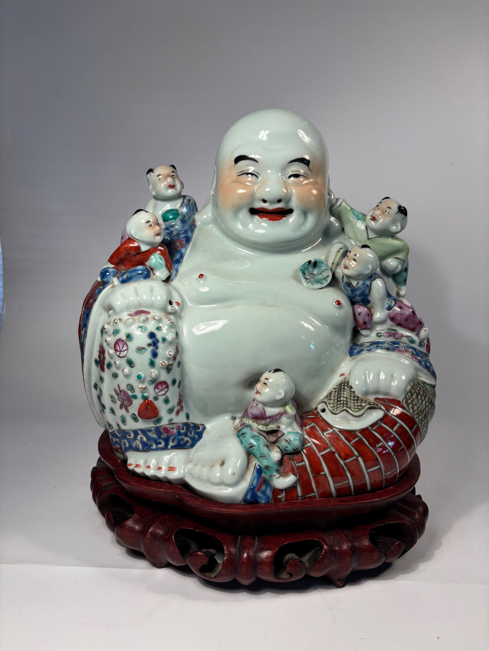 A Large Chinese Famille Rose porcelain Laughing Buddha marked "MAO SHENG JI ZAO" with stand: Early 20th century; A joyful and richly detailed porcelain figure of the Laughing Buddha (Budai) surrounded by five children. Dimensions?Height without stand: 11 inches; Width: 10 inches.