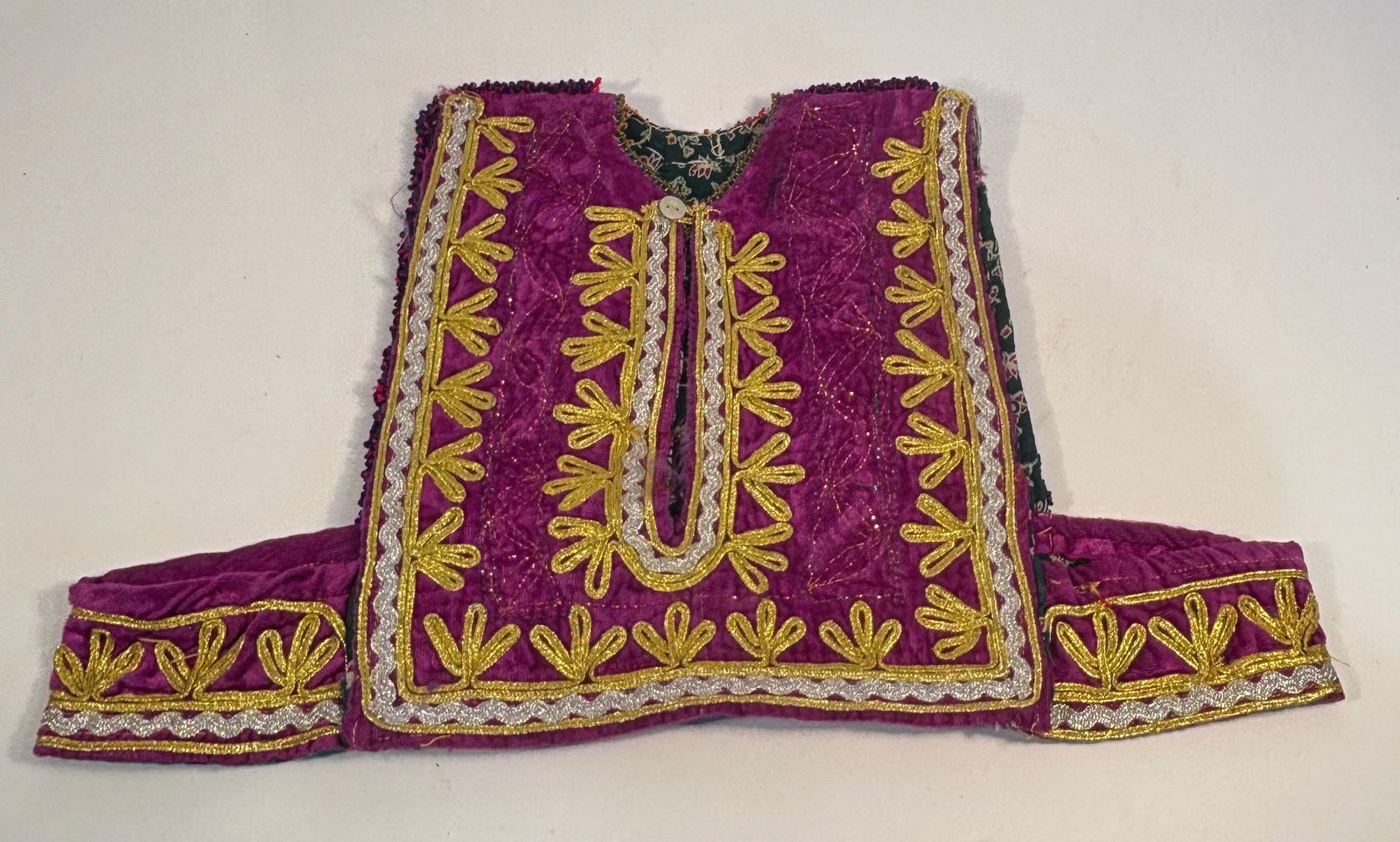 A Traditional Afghan Kuchi Beaded and Embroidered Child’s Vest: Traditional Afghan Kuchi child’s vest, richly adorned with vibrant embroidery and beadwork. The front features deep purple velvet with gold, silver, and yellow thread floral motifs, accented by deco
