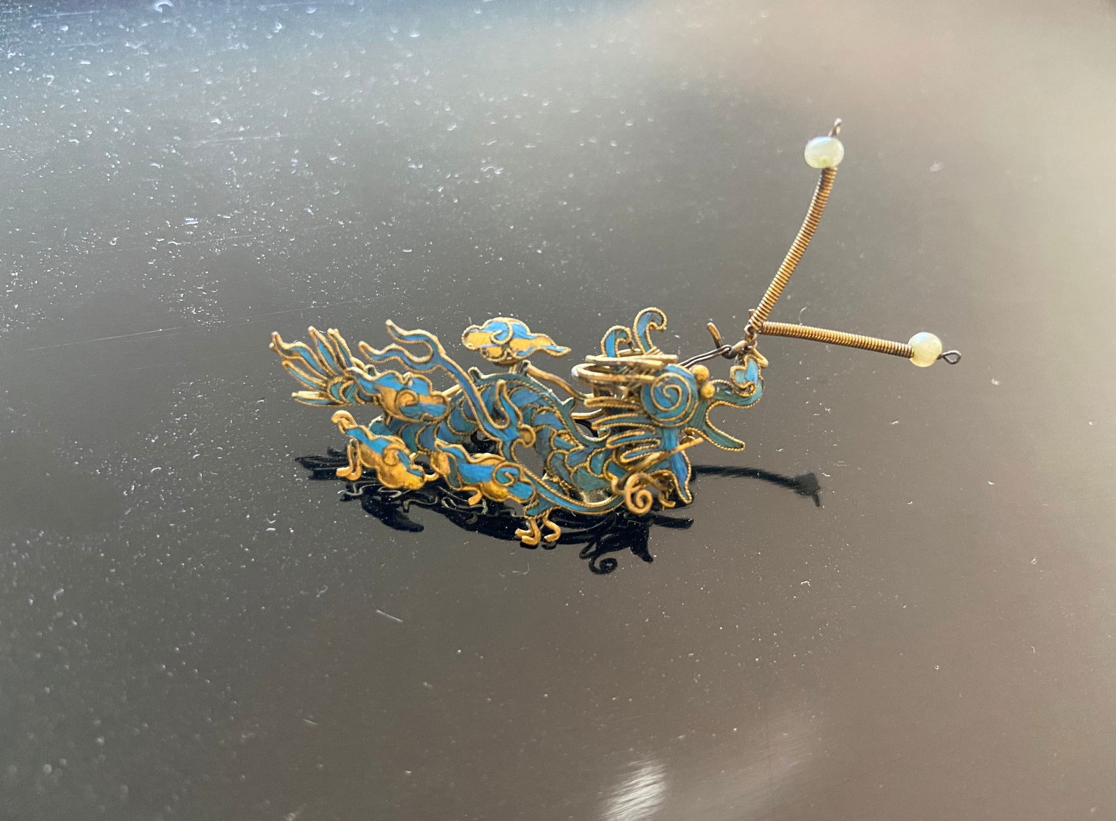 A Chinese Kingfisher feather gilt silver dragon style ornament: Qing Dynasty (1644-1912); Antique ornament feather. It seems to be a dragon with curving, fluid lines that might represent stylized clouds, waves, or flora. Dimensions?Length: 5.5cm