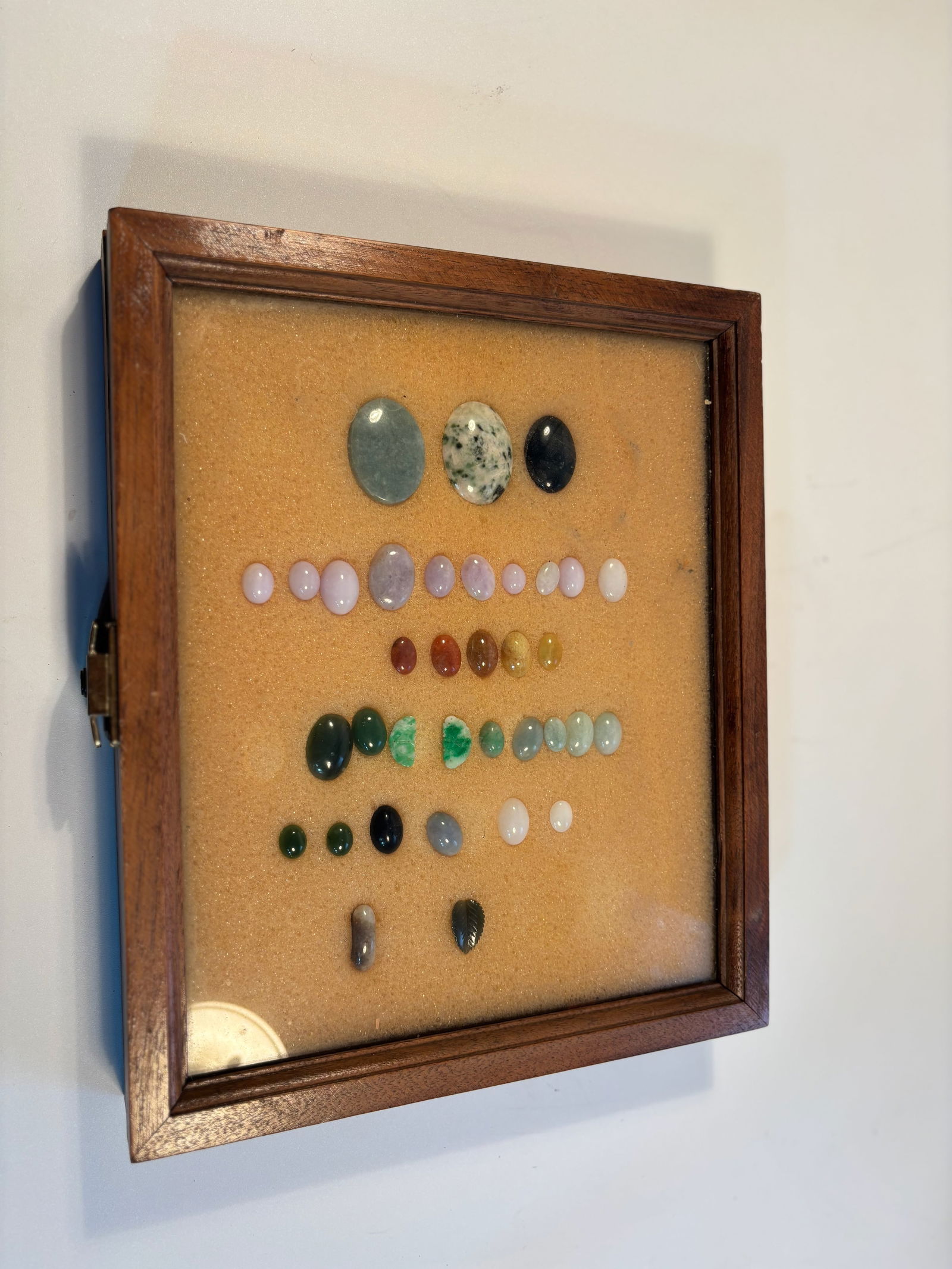 A Collection of 35 pieces jade , lavender jadeite and gemstones: This is a collection of polished and cabochon-cut gemstones displayed in a wooden-framed case. The stones including jade , jadeite and lavender jadeite , vary in color, size, and type.