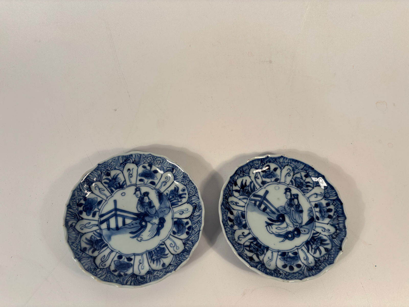 Pair of Chinese blue and white dishes: Kangxi (1662–1722), The central figural scene with two people on a bridge, framed in a cloud cartouche, is a classic Kangxi design; Scalloped rim: Another signature Kangxi-style