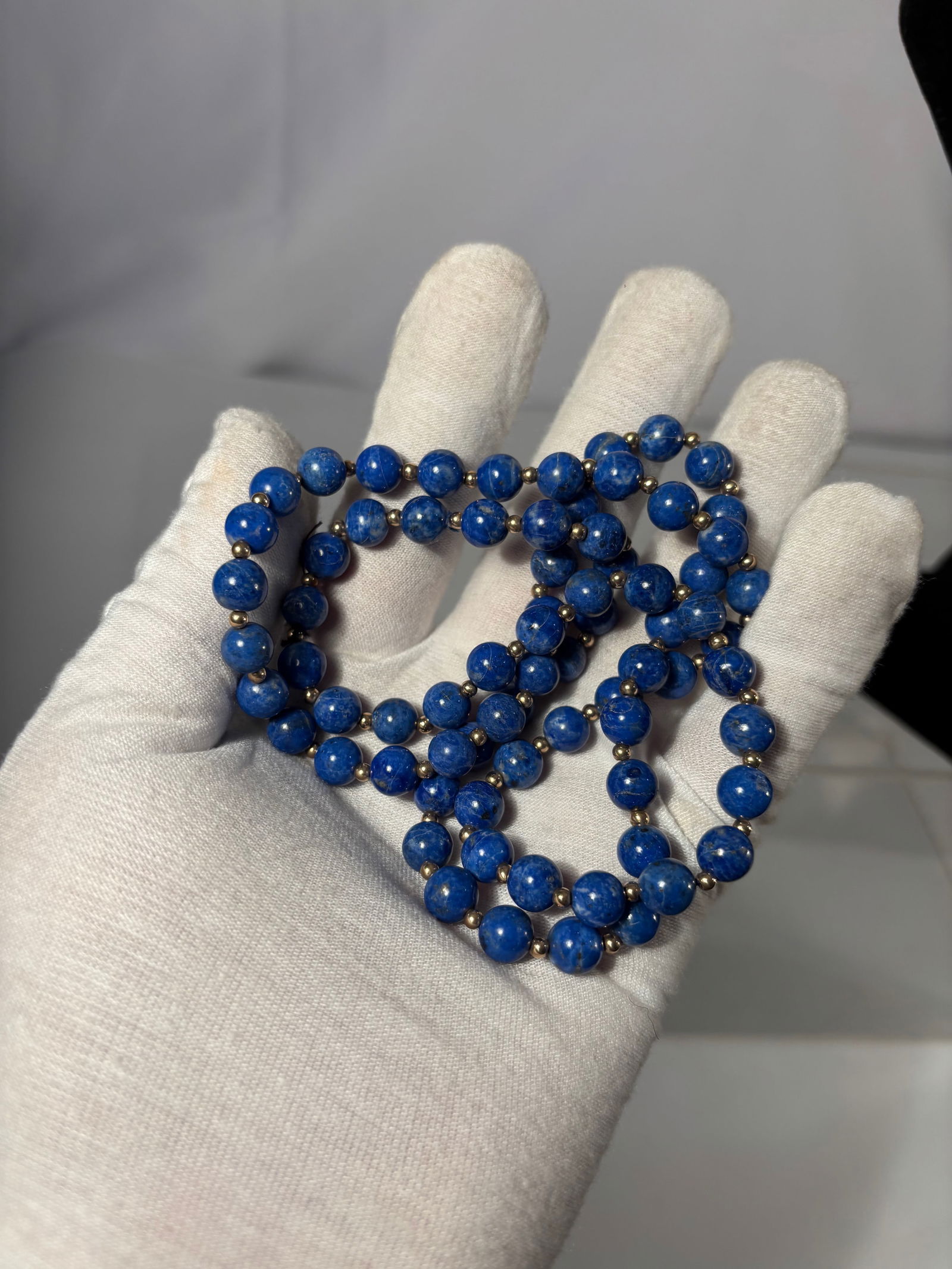 A Natural Lapis Lazuli Bead Necklace with Gold-Tone Spacers: This necklace is composed of natural lapis lazuli round beads, displaying a rich deep blue color with visible natural mineral inclusions and subtle tonal variation characteristic of lapis lazuli. The