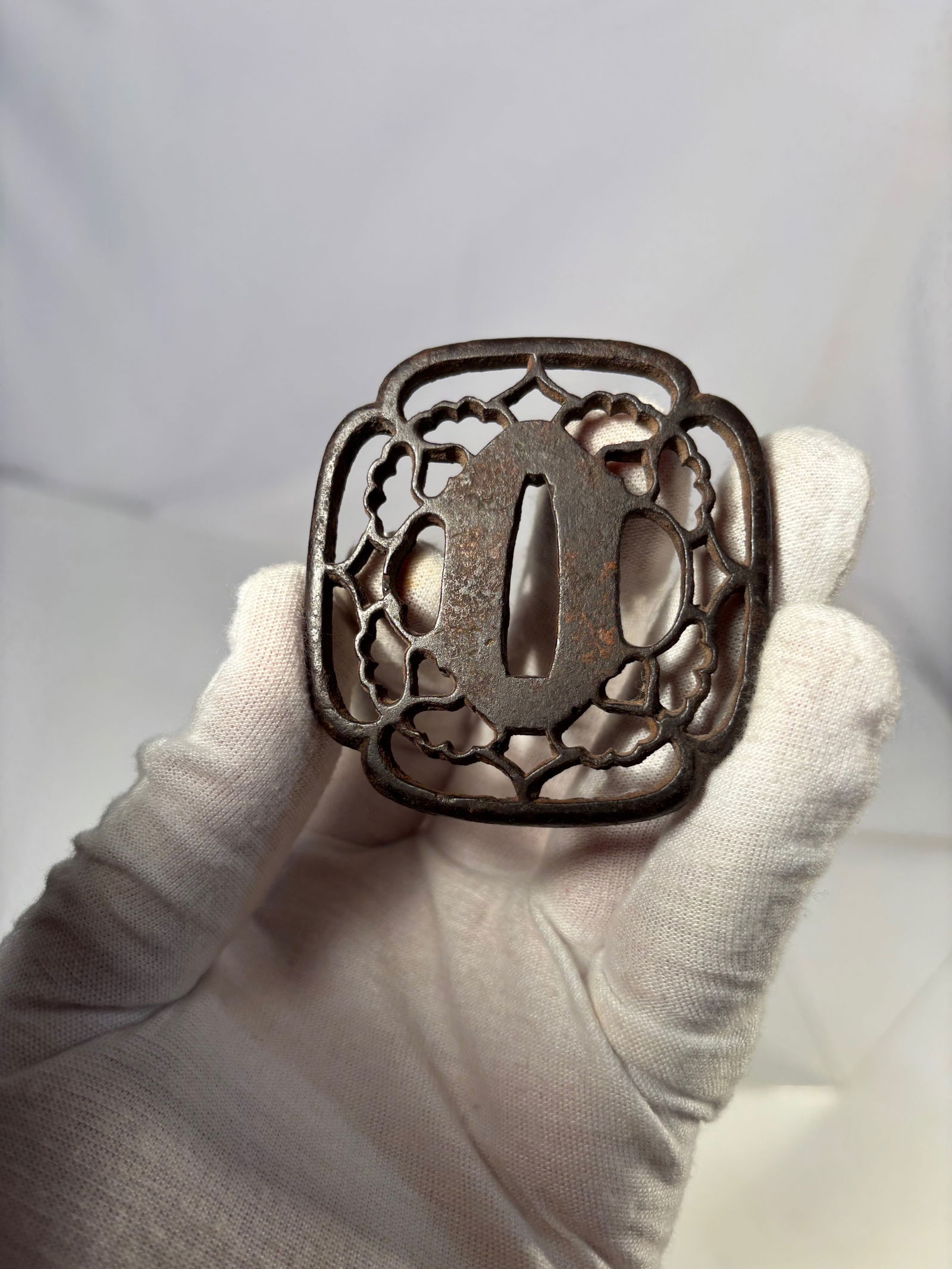 A Japanese Edo Period Iron Sukashi Tsuba with Old Collection Number (Sword Guard), Likely Edo: Japanese iron sukashi tsuba of oval form, featuring openwork floral motifs in symmetrical composition. The iron surface exhibits natural age patina and oxidation. The reverse bears an old painted inve