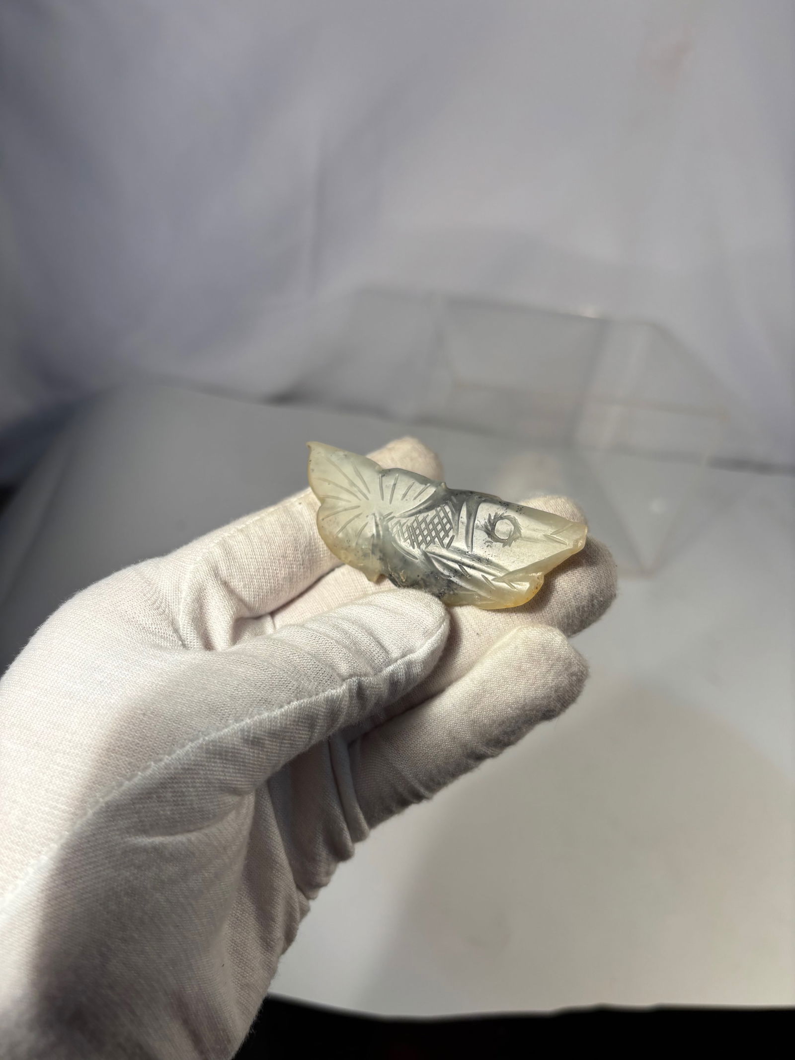 A Chinese Carved Jade Fish Pendant: Qing dynasty(1644-1912); Chinese carved jade pendant in the form of a stylized fish, finely rendered in relief with incised scales, fins, and facial details. The stone displays attractive natural