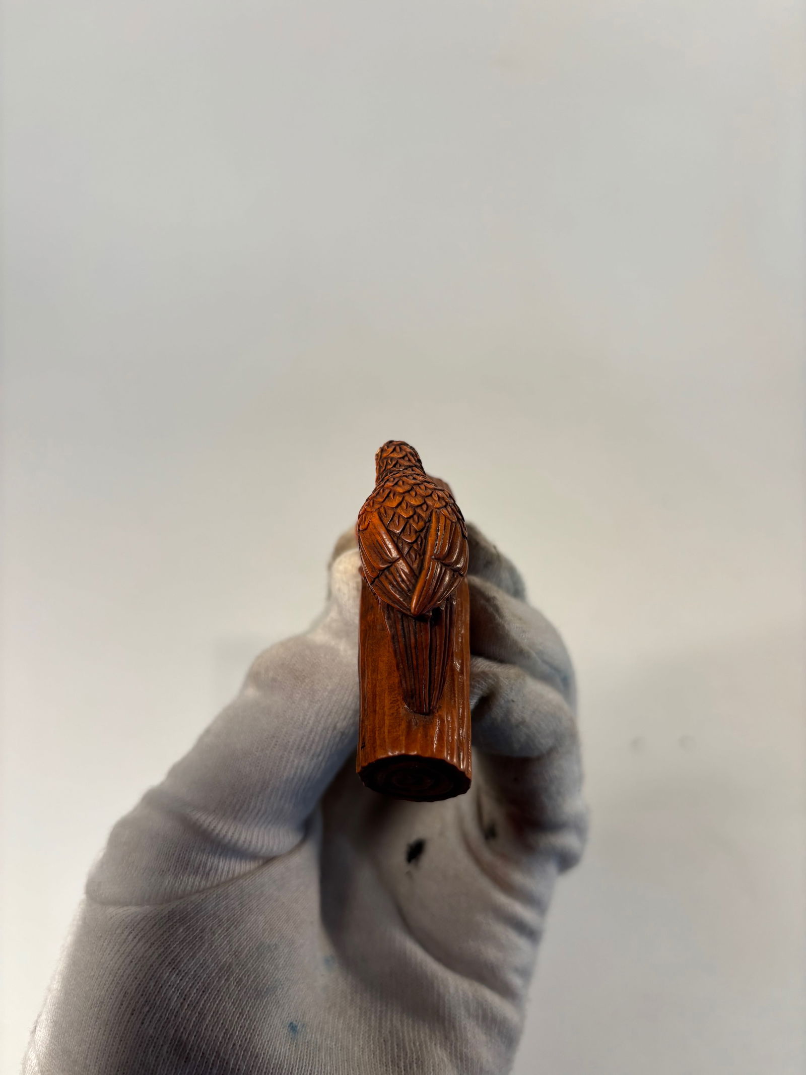 A Japanese Boxwood Netsuke of a Bird on a Branch, Signed Gyokush: Meiji Period or later (late 19th–early 20th century); Finely carved from a single piece of boxwood, the netsuke depicts a bird poised on a gnarled tree branch, its head lowered in a pecking posture.
