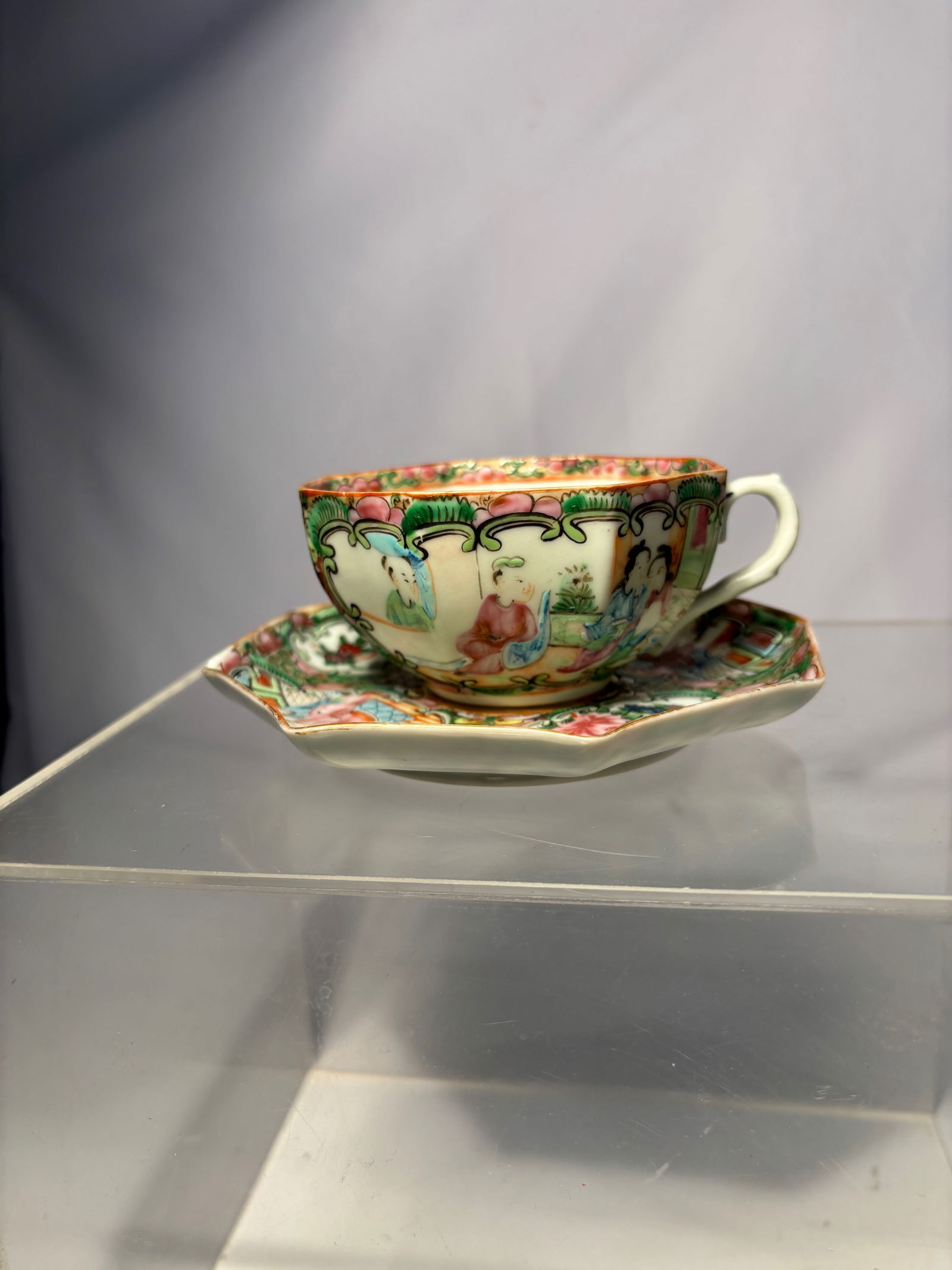 A Chinese Rose Medallion Porcelain Teacup and Octagonal Saucer: Chinese porcelain teacup and matching octagonal saucer decorated in the Rose Medallion style. Featuring alternating panels of court figures and floral-bird motifs in famille rose enamels with green gr