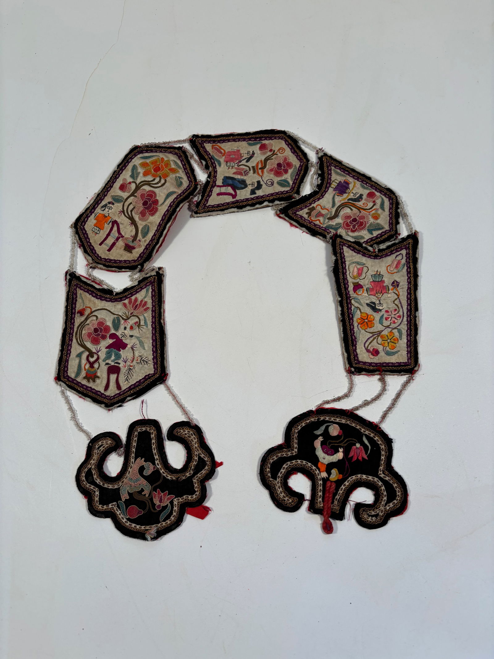 A Chinese silk embroidered ceremonial chain: 19th century;The large, dark cloud-shaped pieces at the base are typical of yunjian design, possibly representing lingzhi.Dimensions? Length: 35 inches.