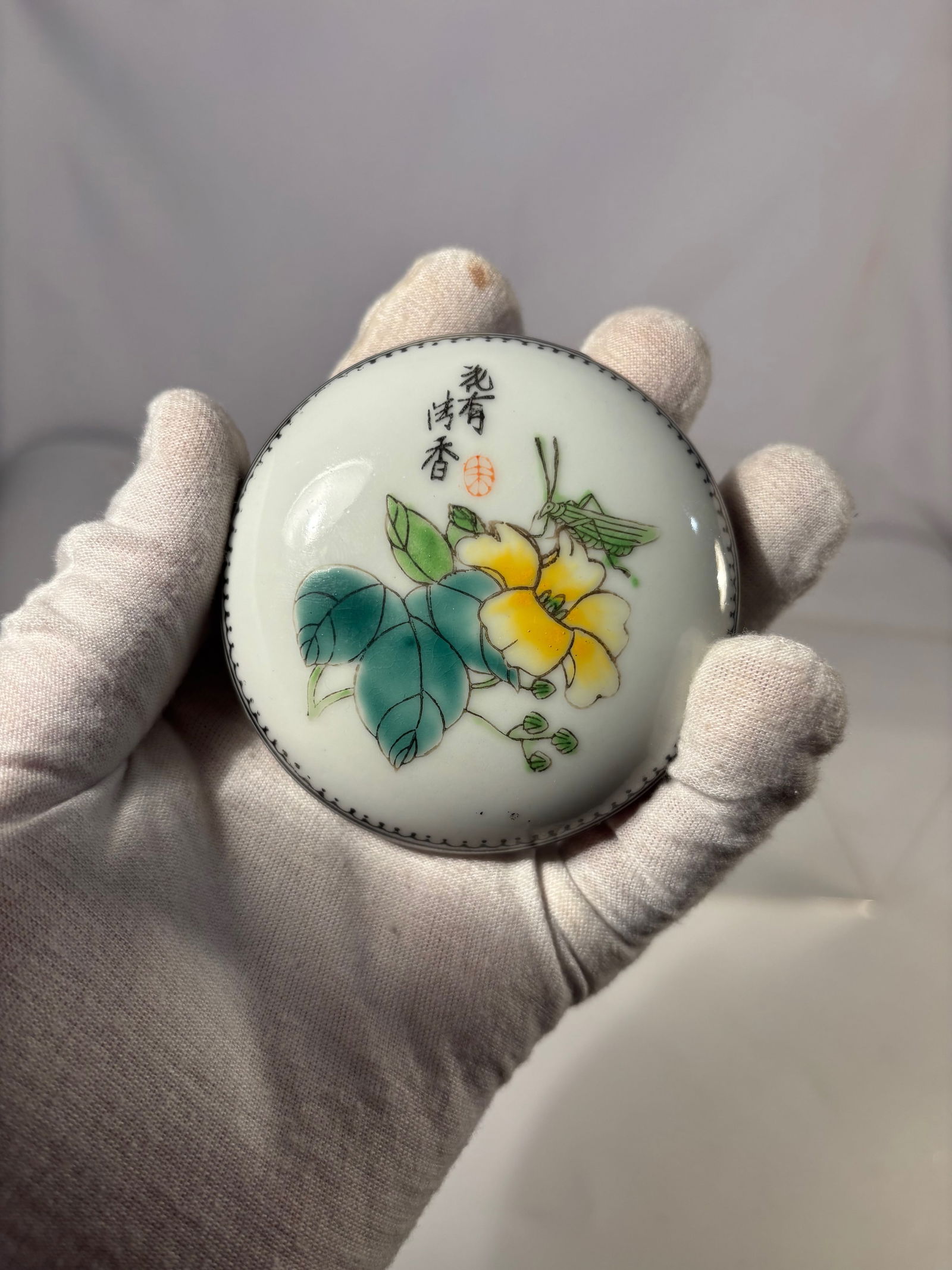 A Chinese Porcelain Covered Box with Floral Decoration, Qianlong Mark: Chinese porcelain covered box decorated with floral motifs and an insect on the lid, accompanied by calligraphy. The base with a red apocryphal Qianlong mark. Diameter: 3.25 inches; Height: 1.5 inches