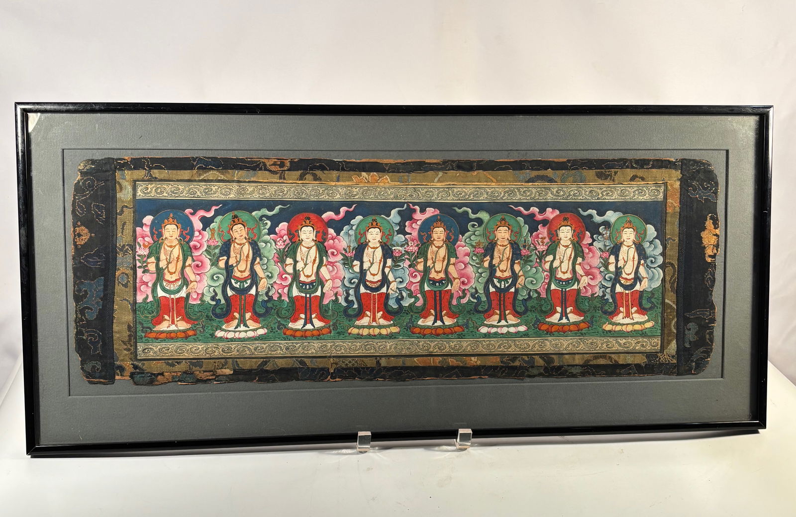 A Himalayan Banner Thangka Depicting Eight Bodhisattvas, Retaining Its Original Two-Layer Silk: (Circa 1880–1930); A horizontal Tibetan banner thangka depicting eight standing bodhisattvas, each shown on lotus bases with vibrant cloud scrolls and colored halos behind them. The painting is exec
