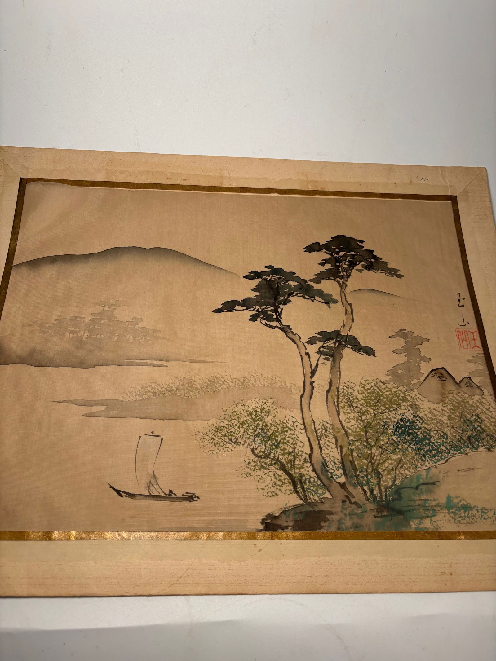 A Japanese Nihonga Watercolor on Silk, Signed Hakuun: 19th century; A serene Japanese watercolor and ink painting on silk, depicting a quiet riverbank scene with tall trees, cottages, and a solitary boatman on still waters. Executed with delicate washes