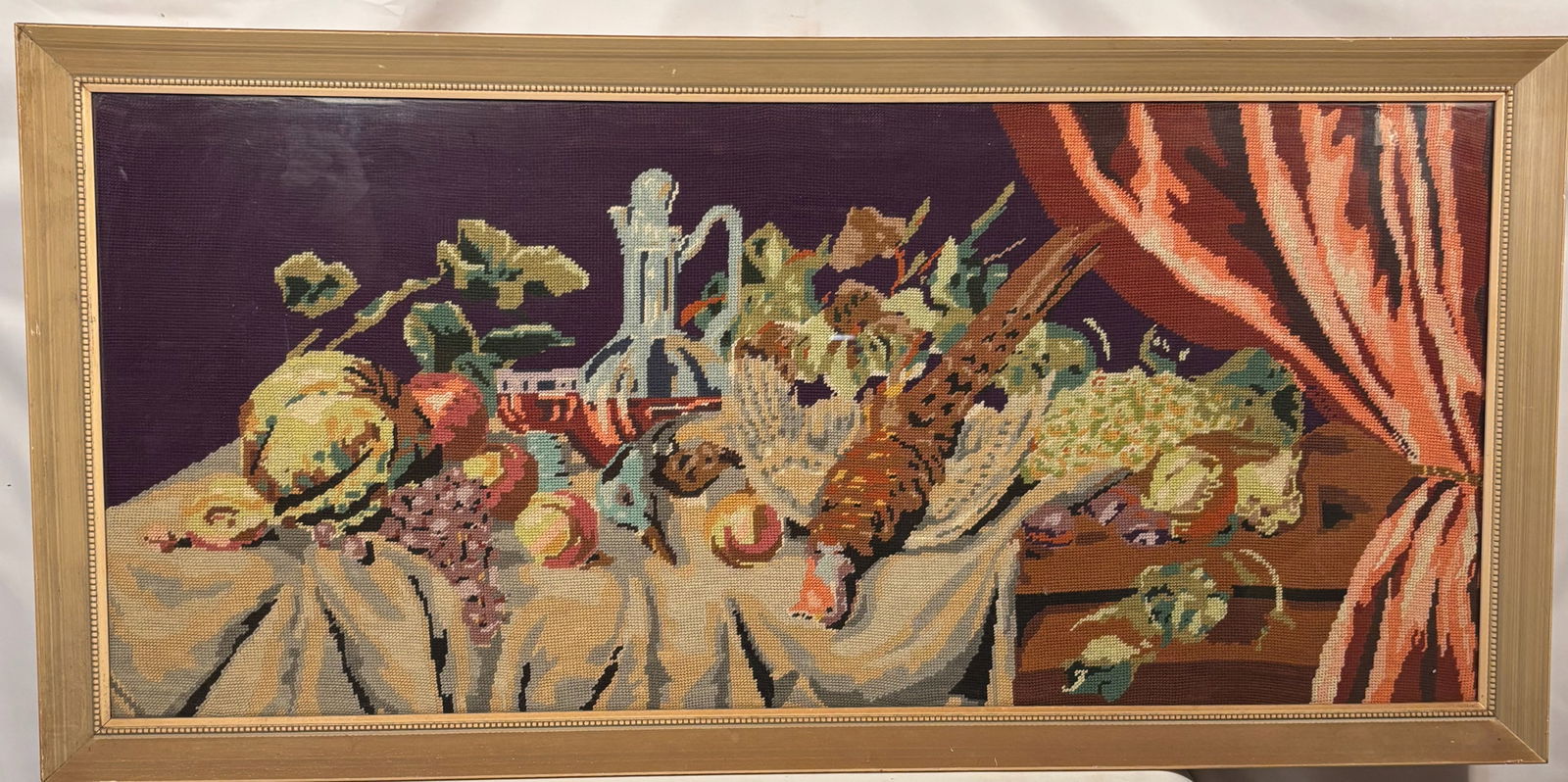 A European Needlepoint Still Life with Game Bird and Fruit: Hand-stitched European needlepoint embroidery depicting a classical still life scene with fruit, grapes, glassware, and a game bird on a draped table, after Old Master hunting still life paintings. Mo