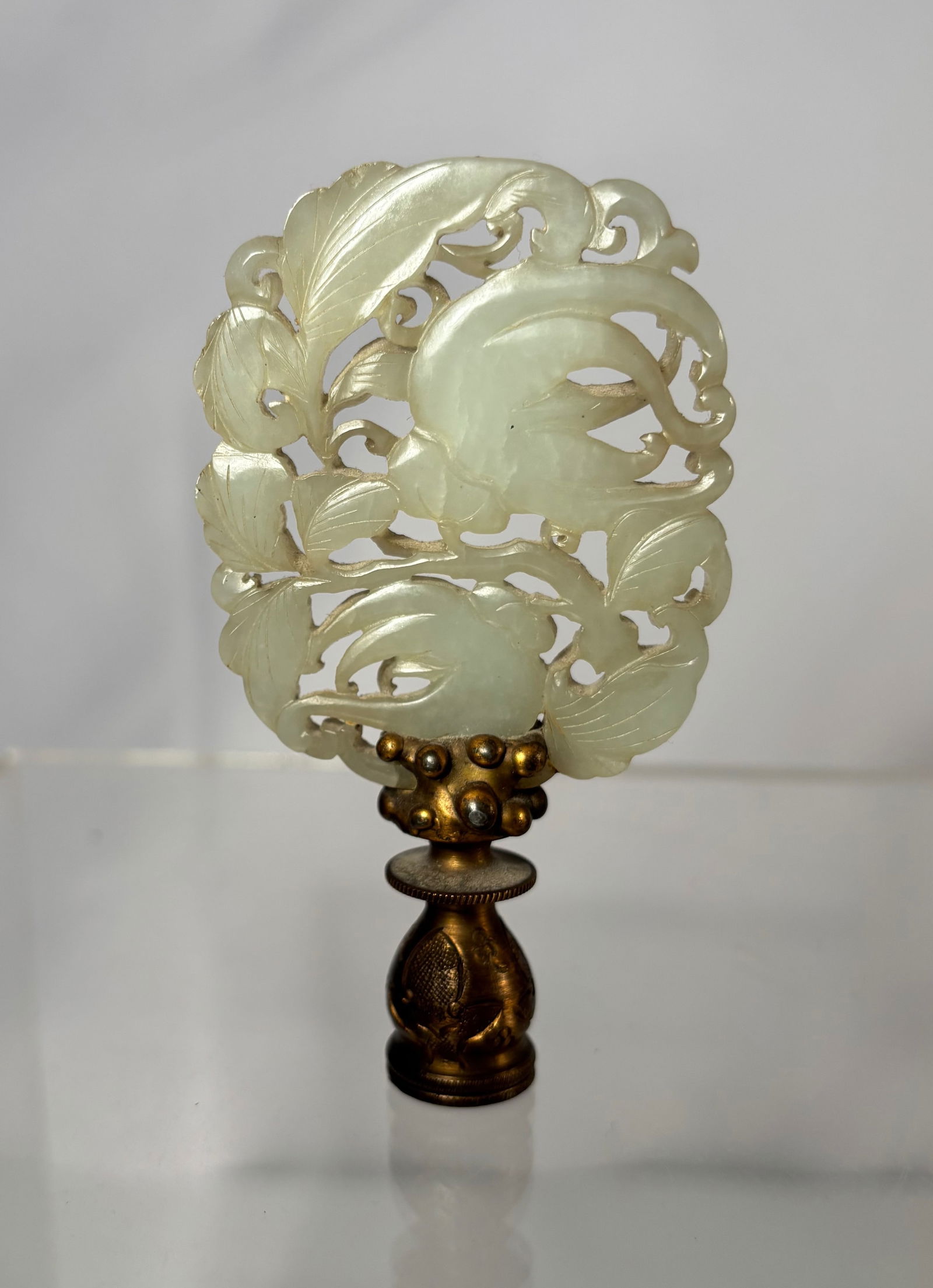A Chinese Carved Celadon Jade Openwork Ornament on Metal Handle: Qing Dynasty (1644-1912) ; Chinese carved celadon jade ornament featuring an openwork scrolling foliate motif. The jade of pale celadon tone with semi-translucent quality and smooth polish. Finely car