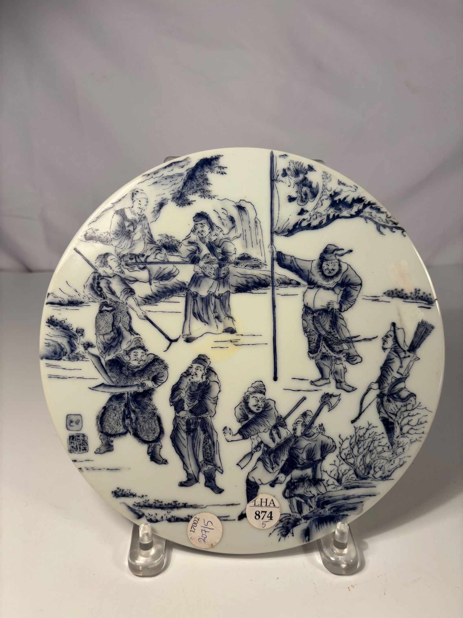 A Chinese Blue Enamel Painted Porcelain Round Plaque with Warrior Scene, Qianlong Mark: Circular Chinese porcelain plaque, painted in varying tones of overglaze blue enamel with a detailed martial scene of warriors in animated poses, some wielding swords and banners, set against a mounta