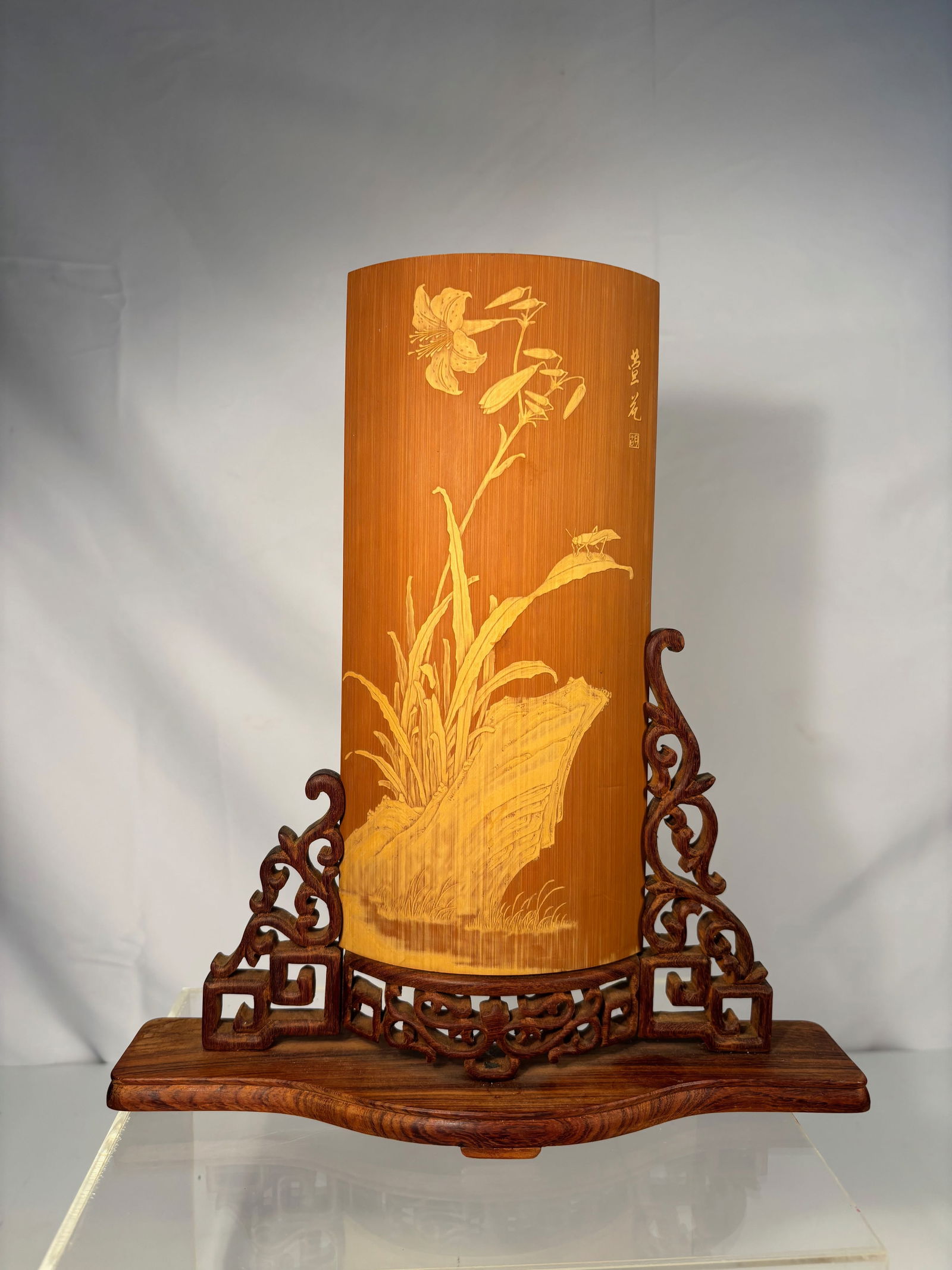 A Chinese Carved Bamboo Armrest (Bi Ge) with Flower and Insect Motif, Signed, with Stand: A finely carved Chinese bamboo armrest (bi ge), delicately worked in relief with blooming flowers and a grasshopper on a leaf. The surface shows warm patina and smooth polish. Inscribed with character