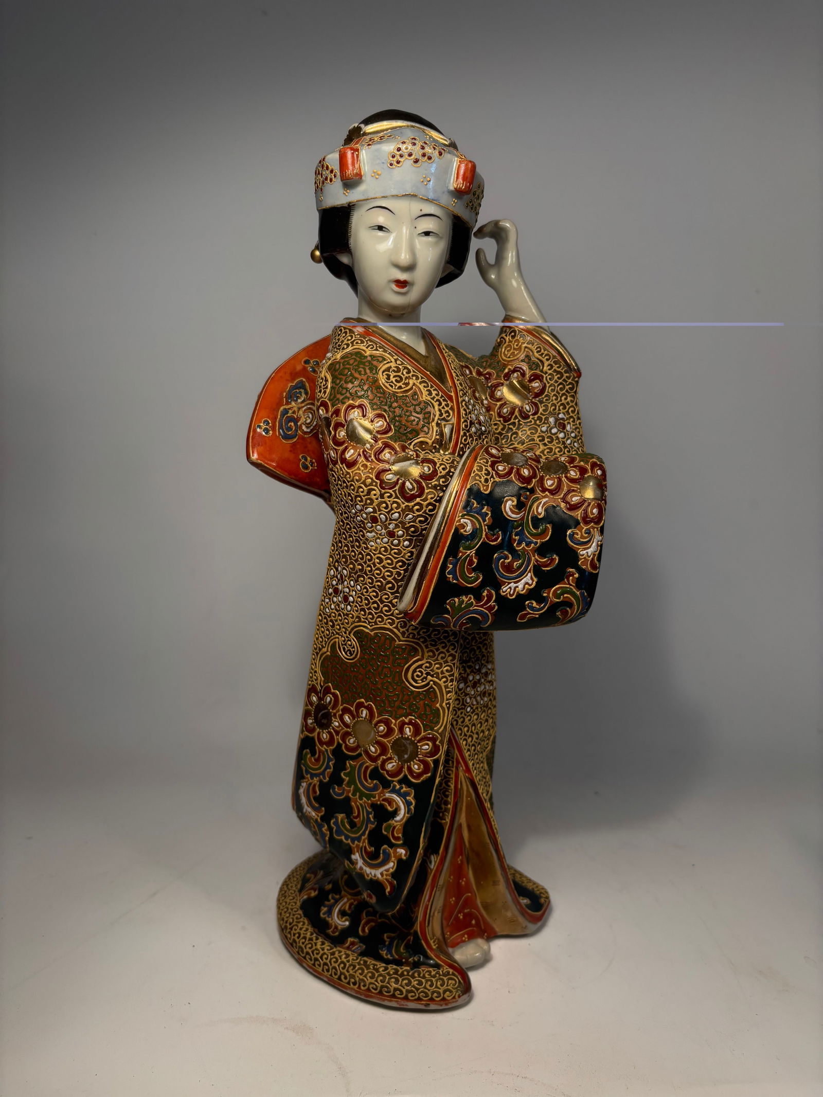 A Japanese Satsuma Moriage Porcelain Geisha Figure: Meiji Period(19th century); A finely modeled and richly decorated Japanese porcelain figure of a Geisha, dating to the Meiji period (late 19th century). The figure is adorned in an elaborate kimono wi